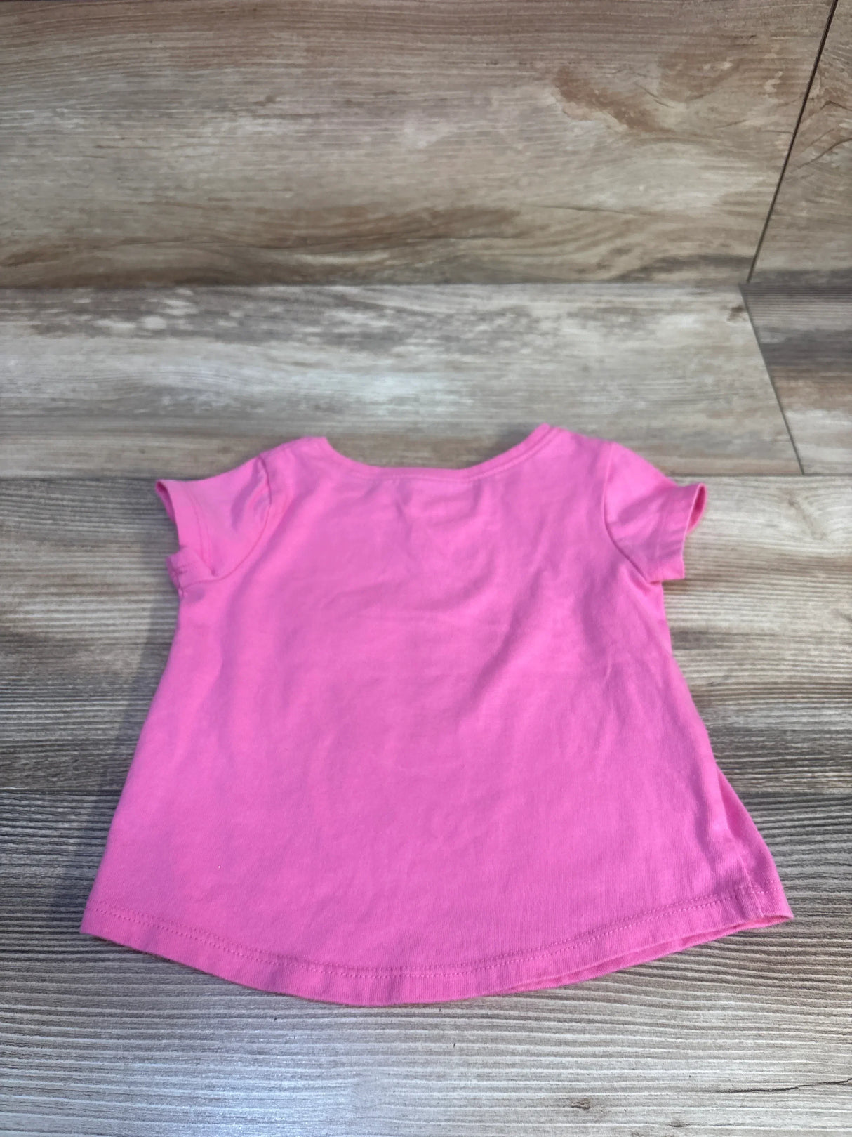 Back view of Jumping Beans Best Sister shirt in pink, showcasing short sleeves and curved hem on wood-grain background