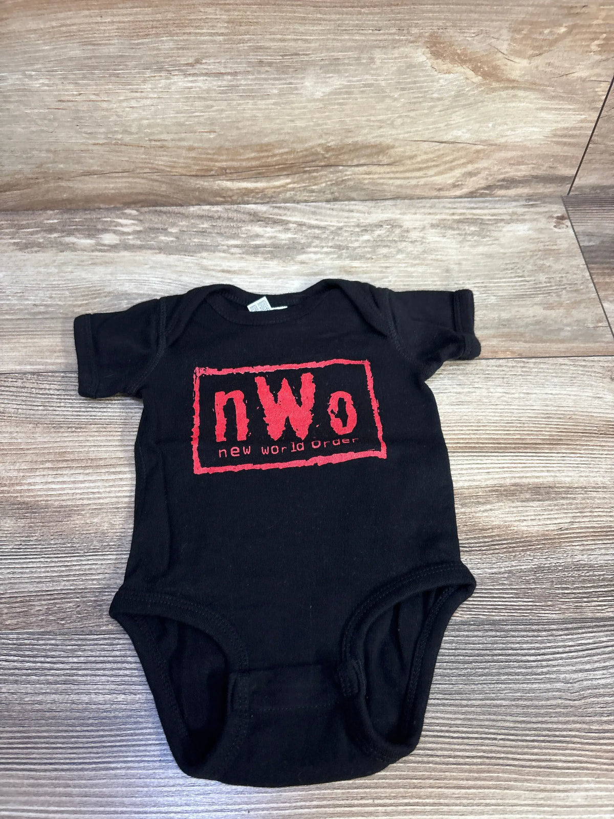 Front view of black Rabbit Skins bodysuit showcasing red NWO New World Order graphic on a wooden floor
