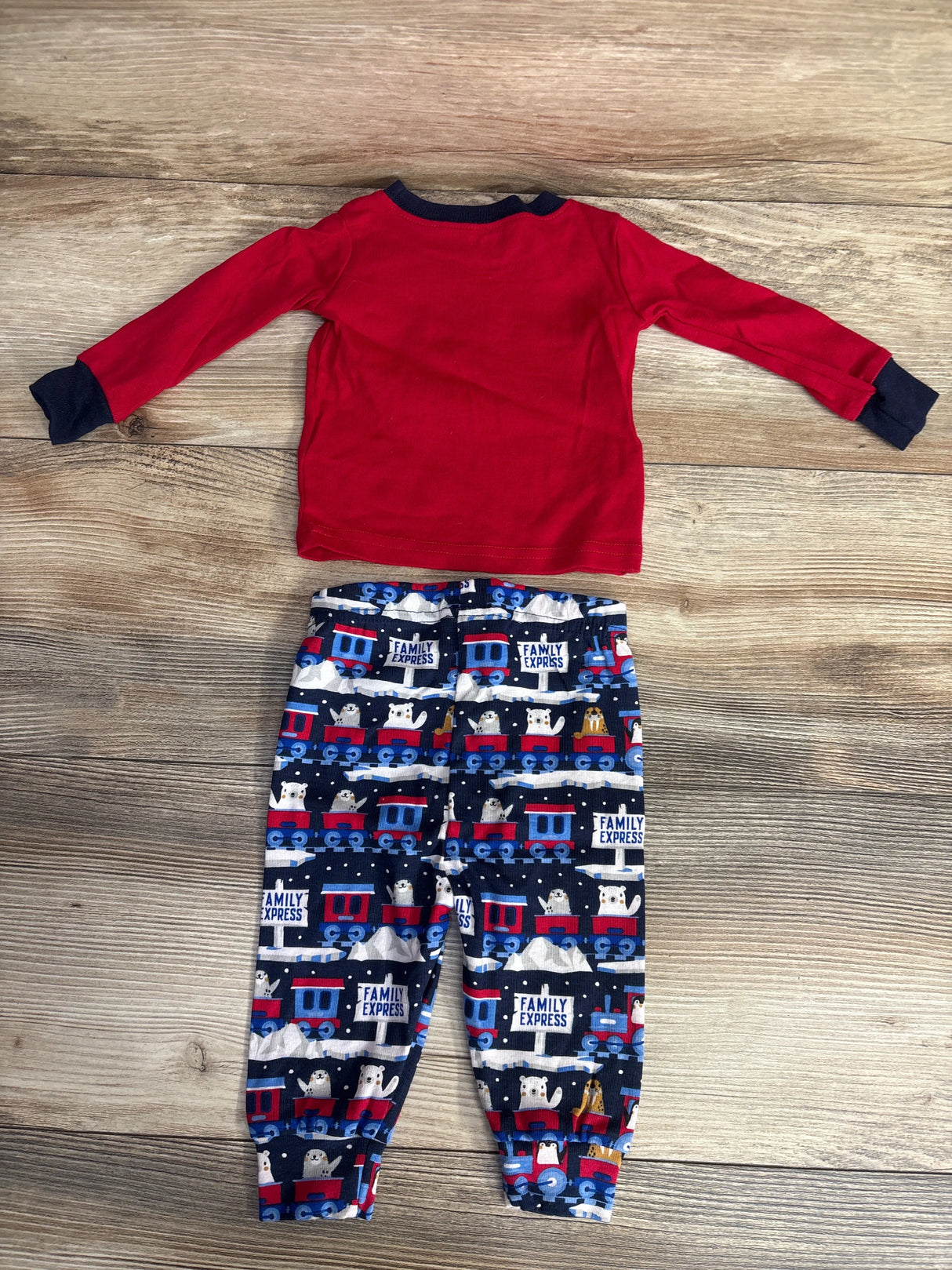 Children's red long-sleeve shirt with navy cuffs and colorful train and animal print pants on wood floor