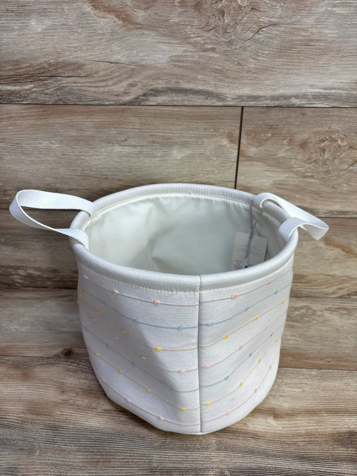 Angled top view of Cloud Island medium round fabric bin with slub stitching, pastel dots, side handles on wood background