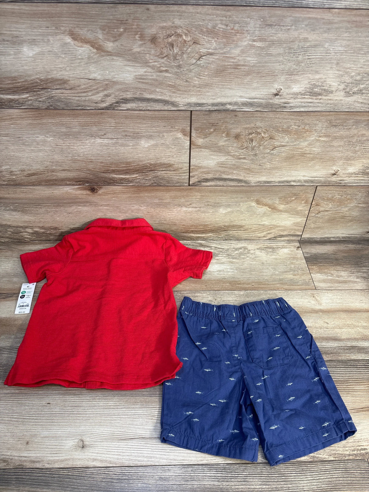 Red polo shirt and navy shark-print shorts for toddler boy, size 4T, laid on wood floor