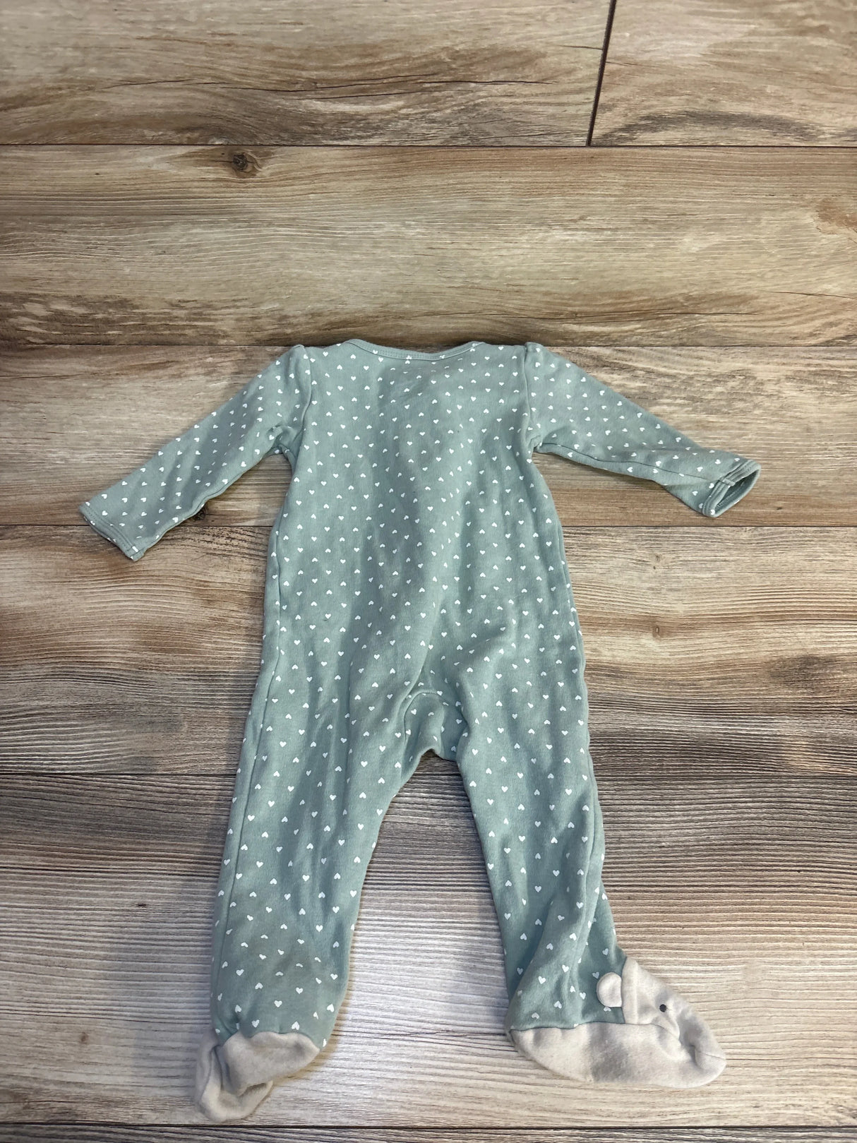 Flat lay of Carter's sage green footed sleeper showing white heart print and bear-face footies on wood floor