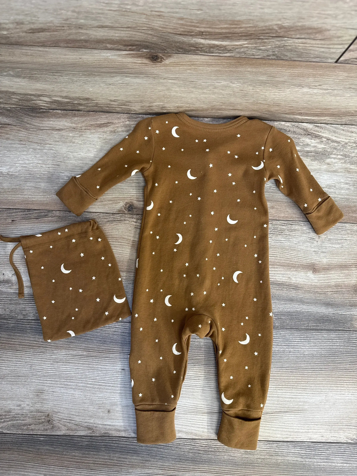 Flat lay of brown snap sleeper with white moon-and-star print and matching drawstring bag on light wood background