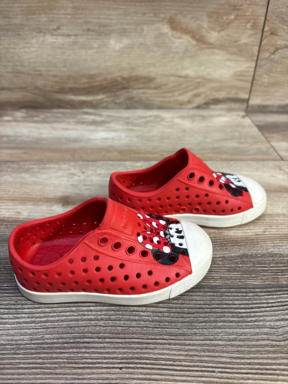 Side view of red Disney Jefferson toddler slip-on shoes showing Minnie Mouse on white toe cap on wood floor