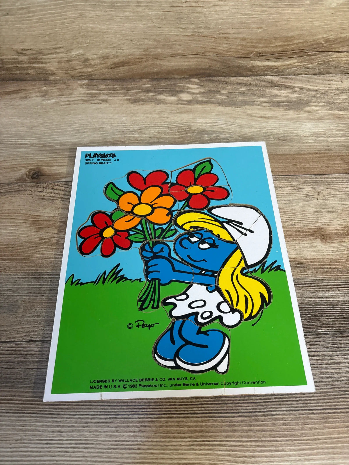 Vintage Smurfette puzzle holding colorful flowers on a wooden surface, kids toy collectible