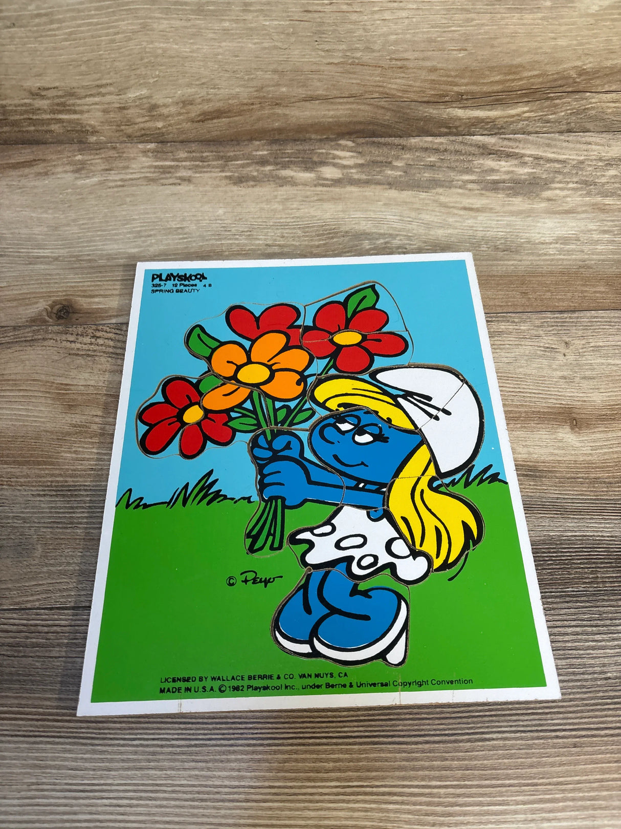 Vintage Smurfette puzzle holding colorful flowers on a wooden surface, kids toy collectible