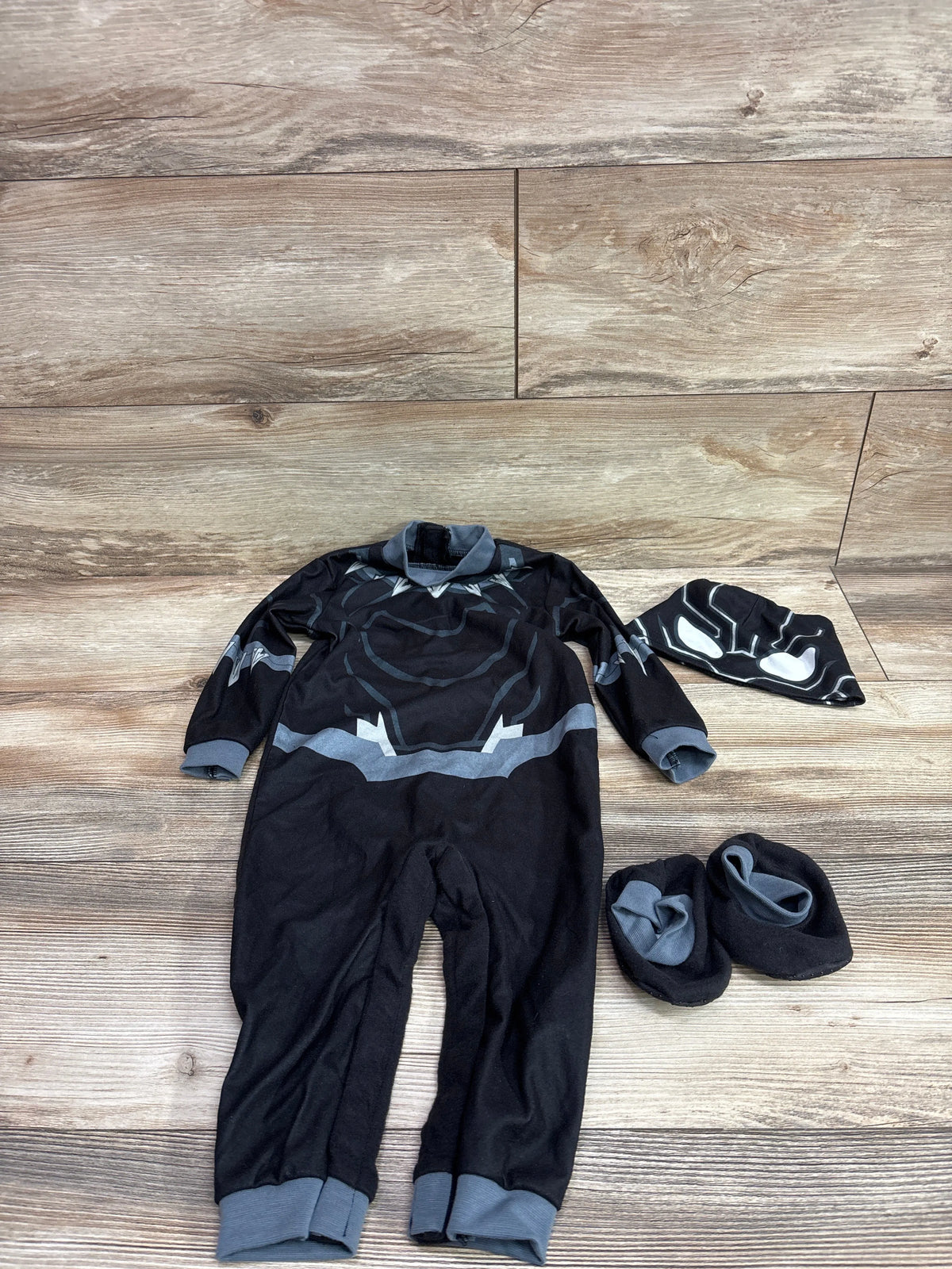 Top view of Black Panther 3pc costume with graphic jumpsuit, matching headpiece, and booties on a wood floor