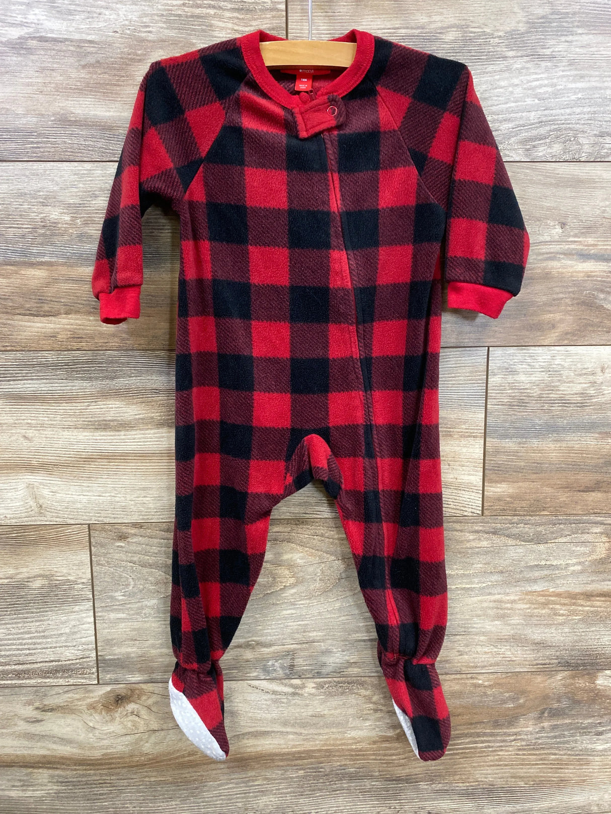 Red and black plaid footed baby sleeper with long sleeves on wooden background