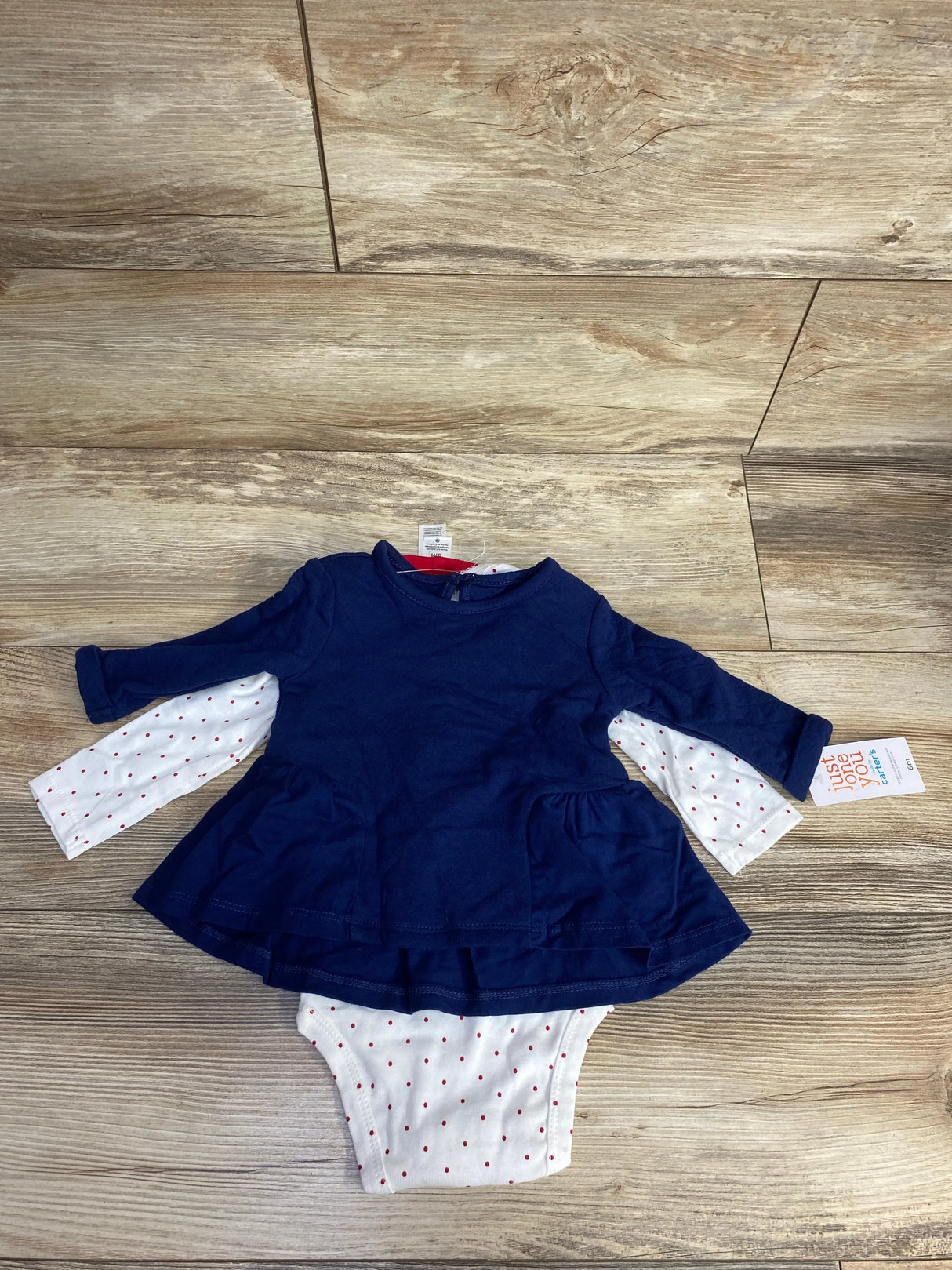 Navy blue long-sleeve baby dress with white polka dot bodysuit on wooden floor