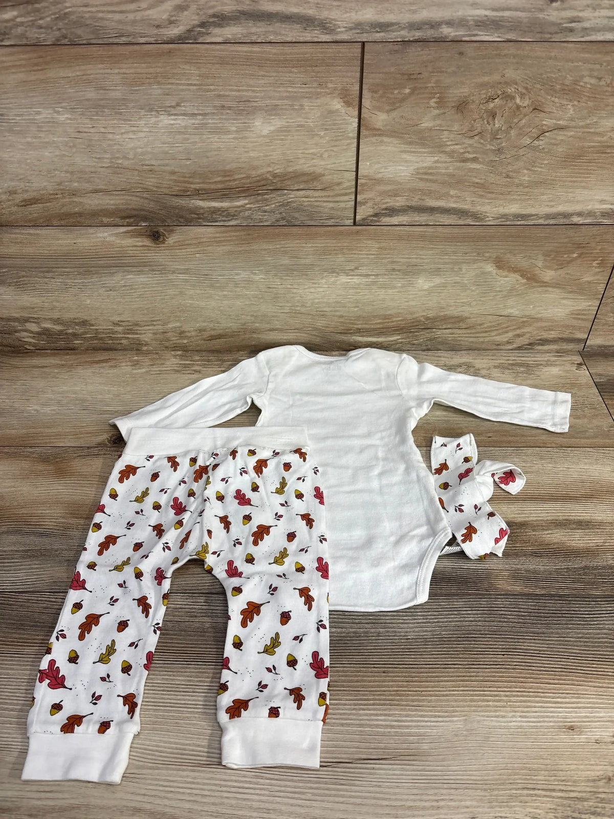 Baby fall-themed outfit with leaf print pants, white onesie, and matching headband on wood floor