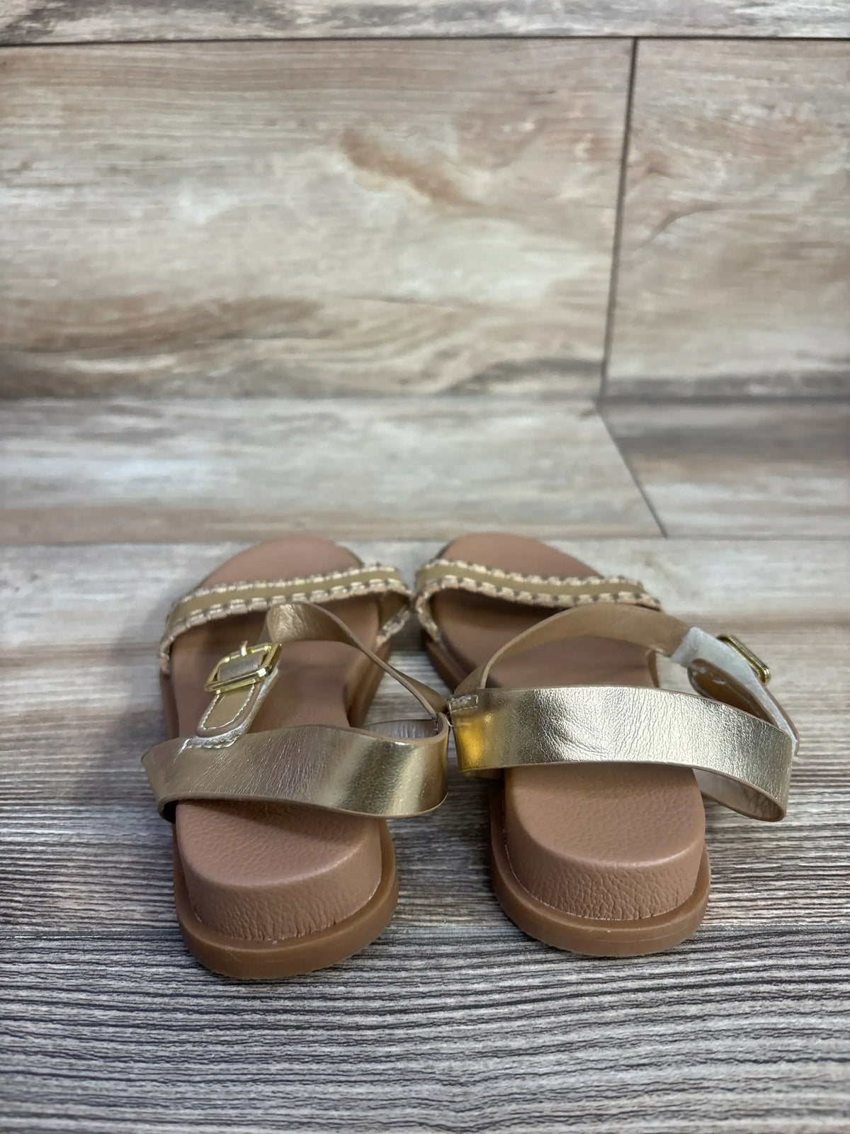 Front view of MIA Peyton size 8C gold sandal with metallic toe strap, braided ankle strap, buckle on wood background