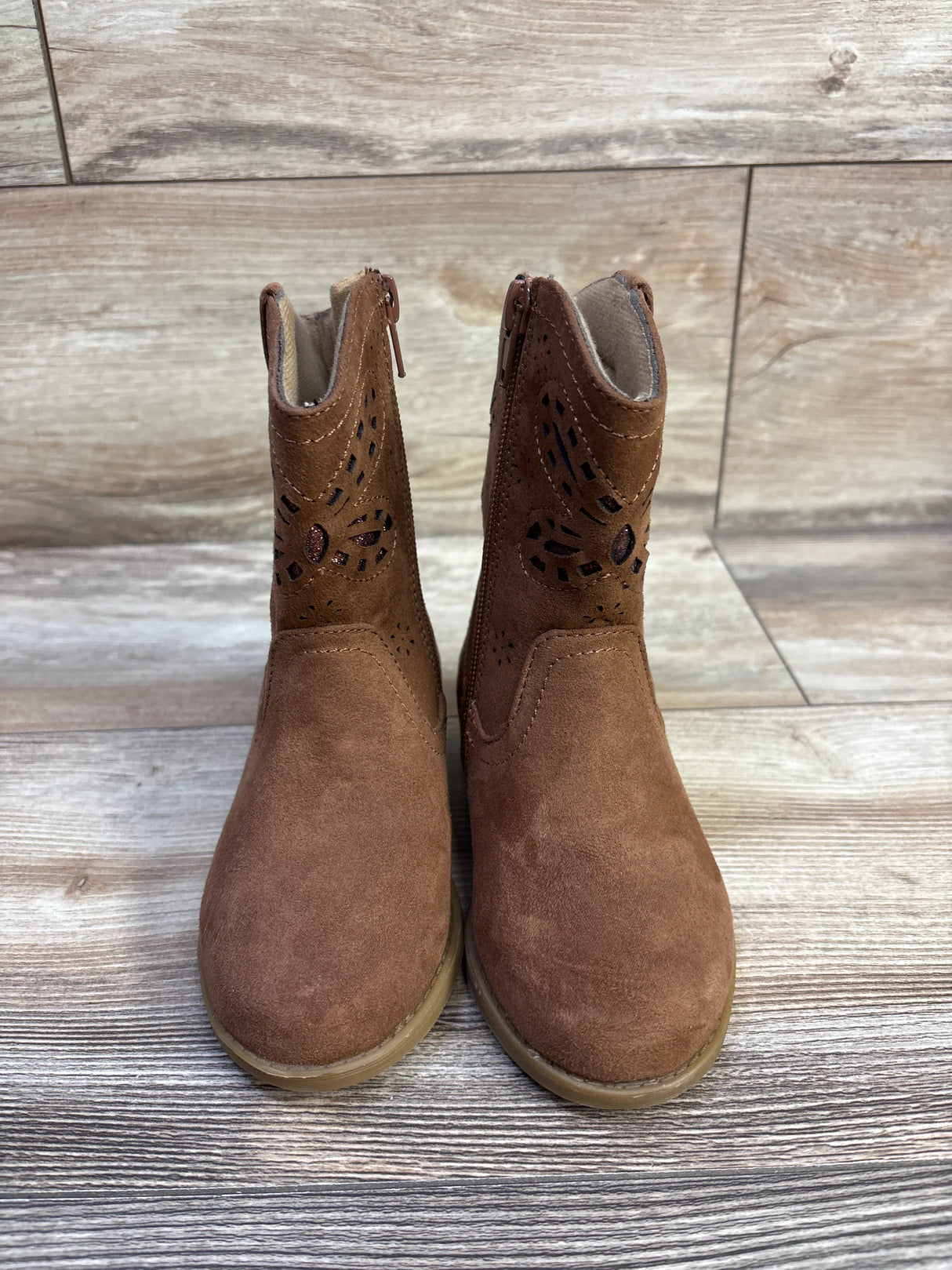 Front view of Lil Jayla toddler brown western boots showcasing laser-cut upper and side zippers on wood floor background