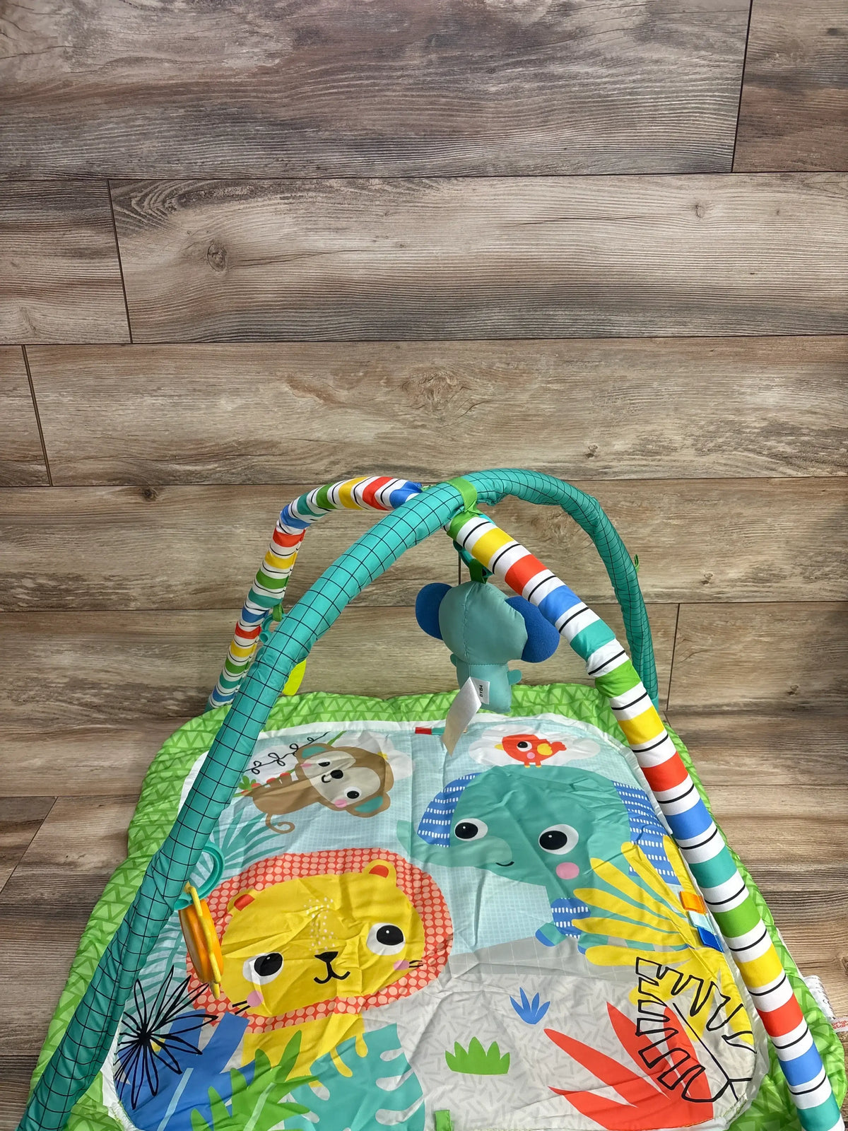 Angled top view of Bright Starts Wild Wiggles play mat with striped arches, hanging toy, and jungle prints on wooden floor