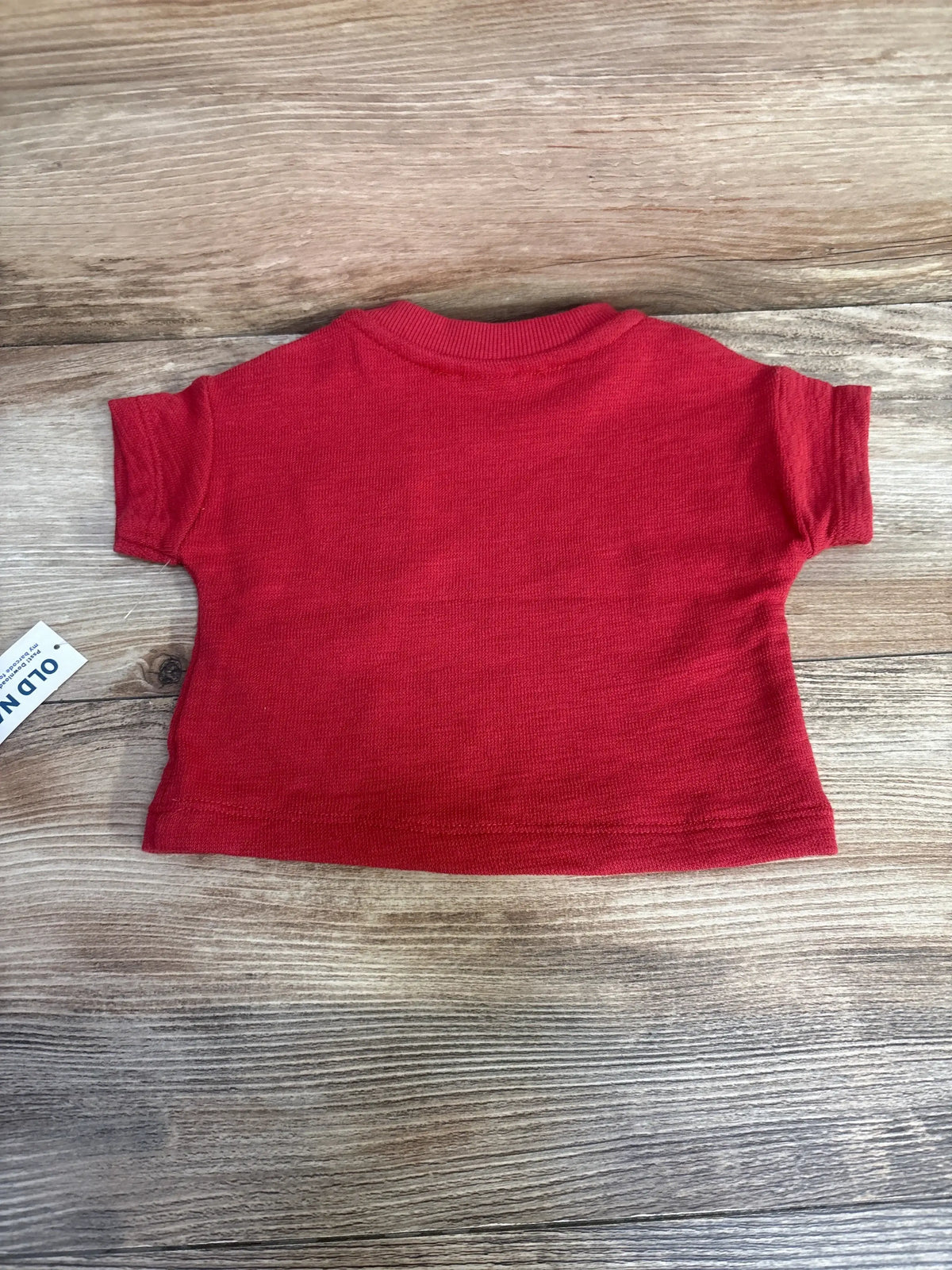 Flat lay of red Old Navy newborn short-sleeve shirt (0-3M) showing back view, ribbed collar and knit texture on wood background