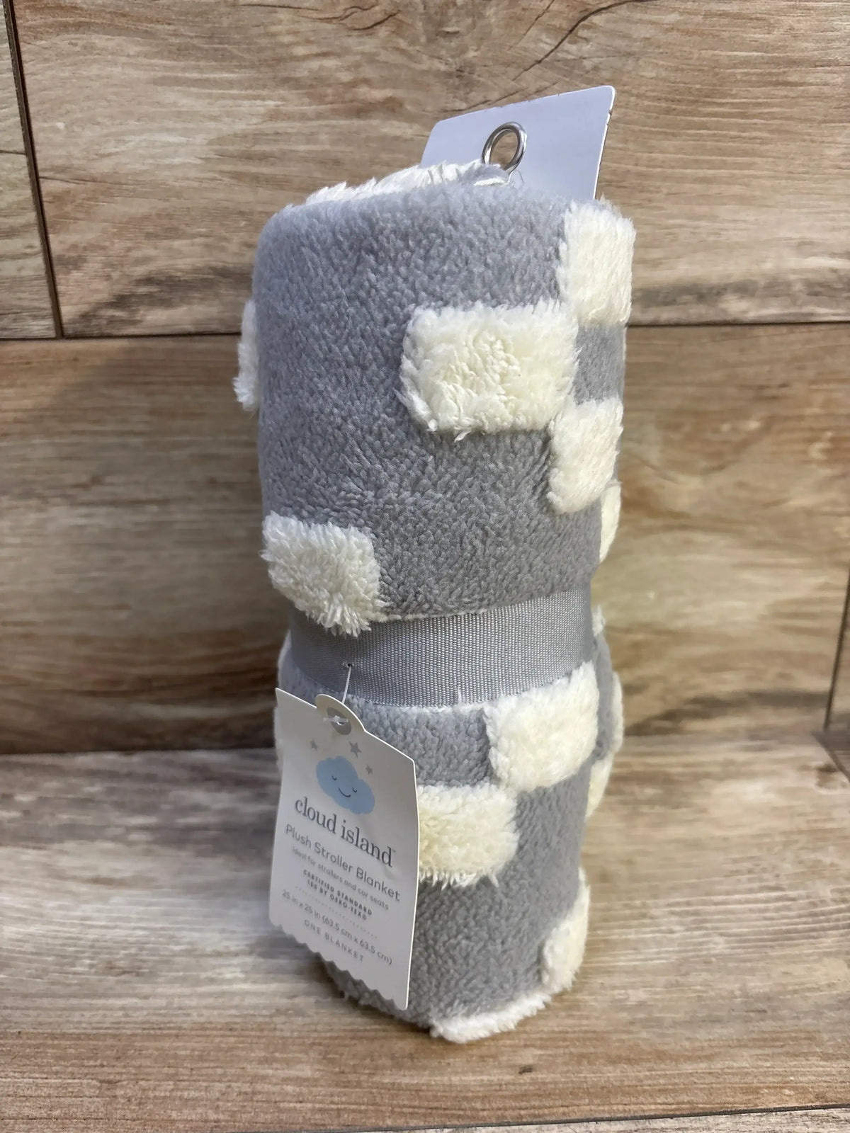 Rolled Cloud Island plush stroller blanket showing gray fabric with cream tufted geometric squares on wood background