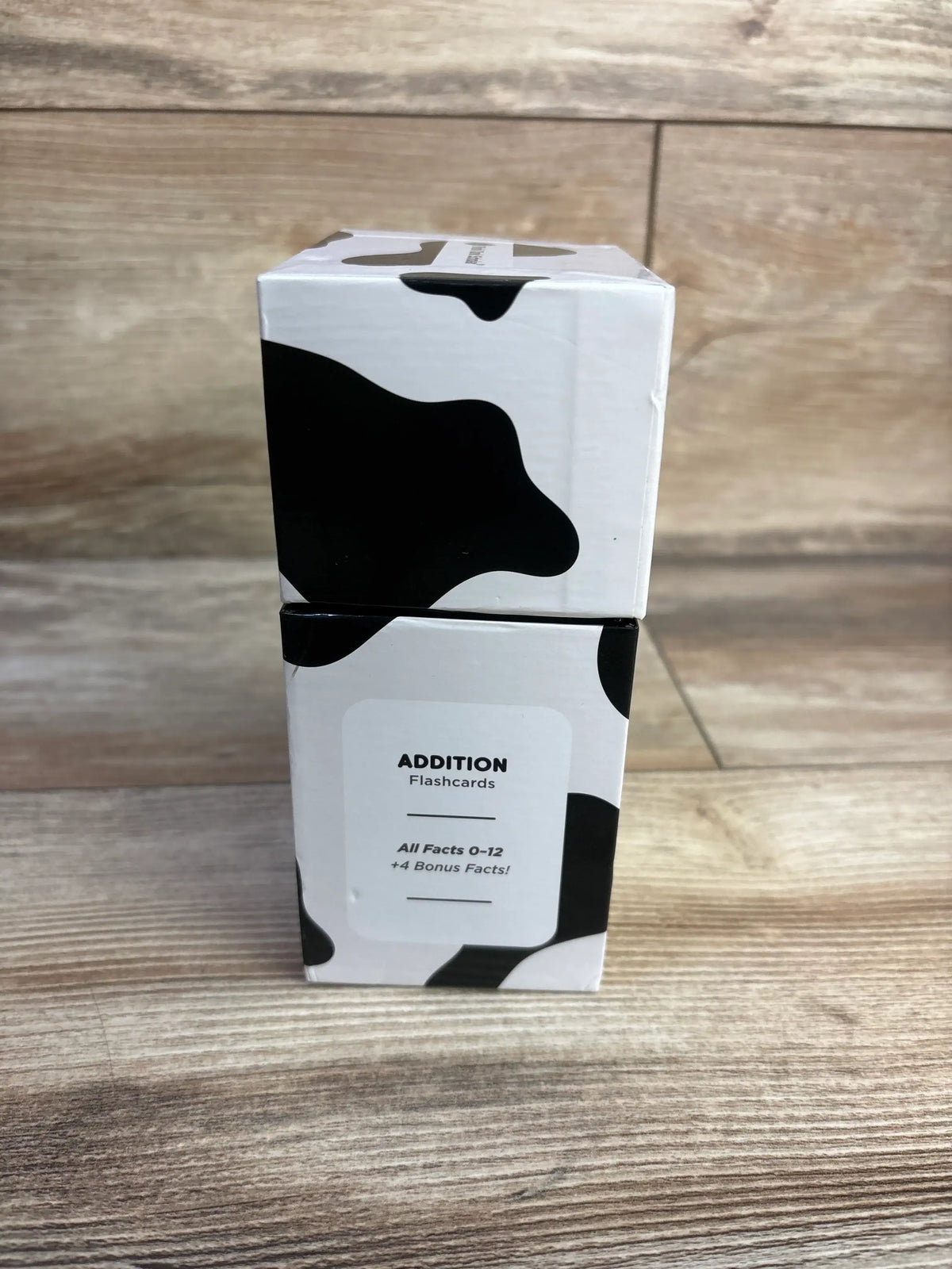 Front view of two stacked Think Tank Scholar Addition flashcards boxes showing cow-print packaging and label on wood floor