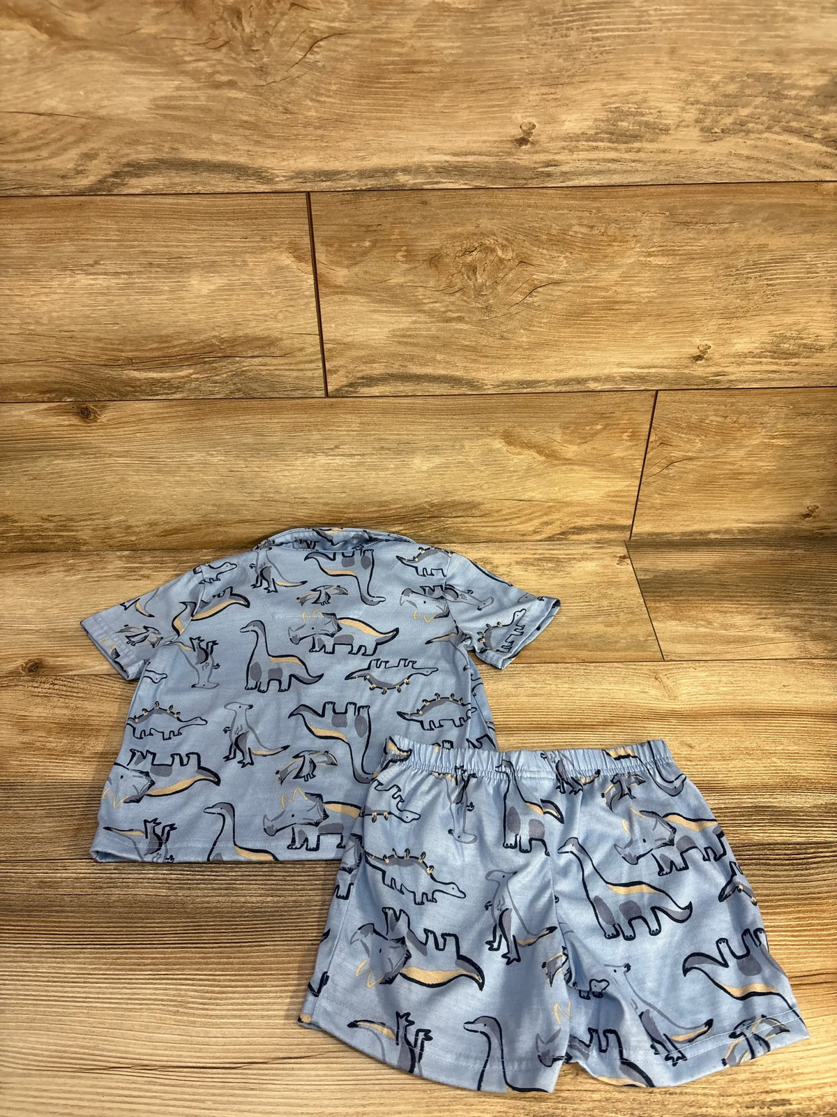 Top-down view of Carter’s blue two-piece pajama set showcasing dinosaur print and matching bottoms on a wood background