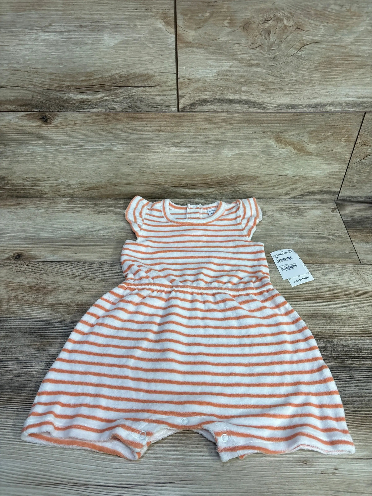 Flat lay of white terry toddler romper with orange stripes, flutter sleeves, elastic waist and snap crotch on wood background