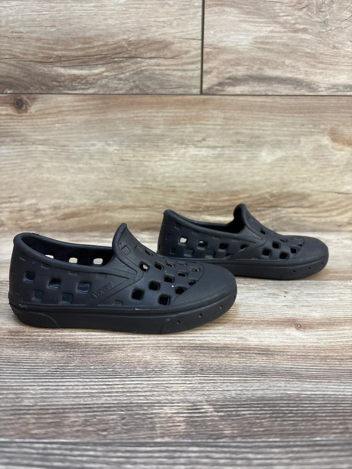 Three-quarter view of Vans Slip-On TRK sandals, size 8C, showcasing rubber slip-on design with square cutouts on wood background