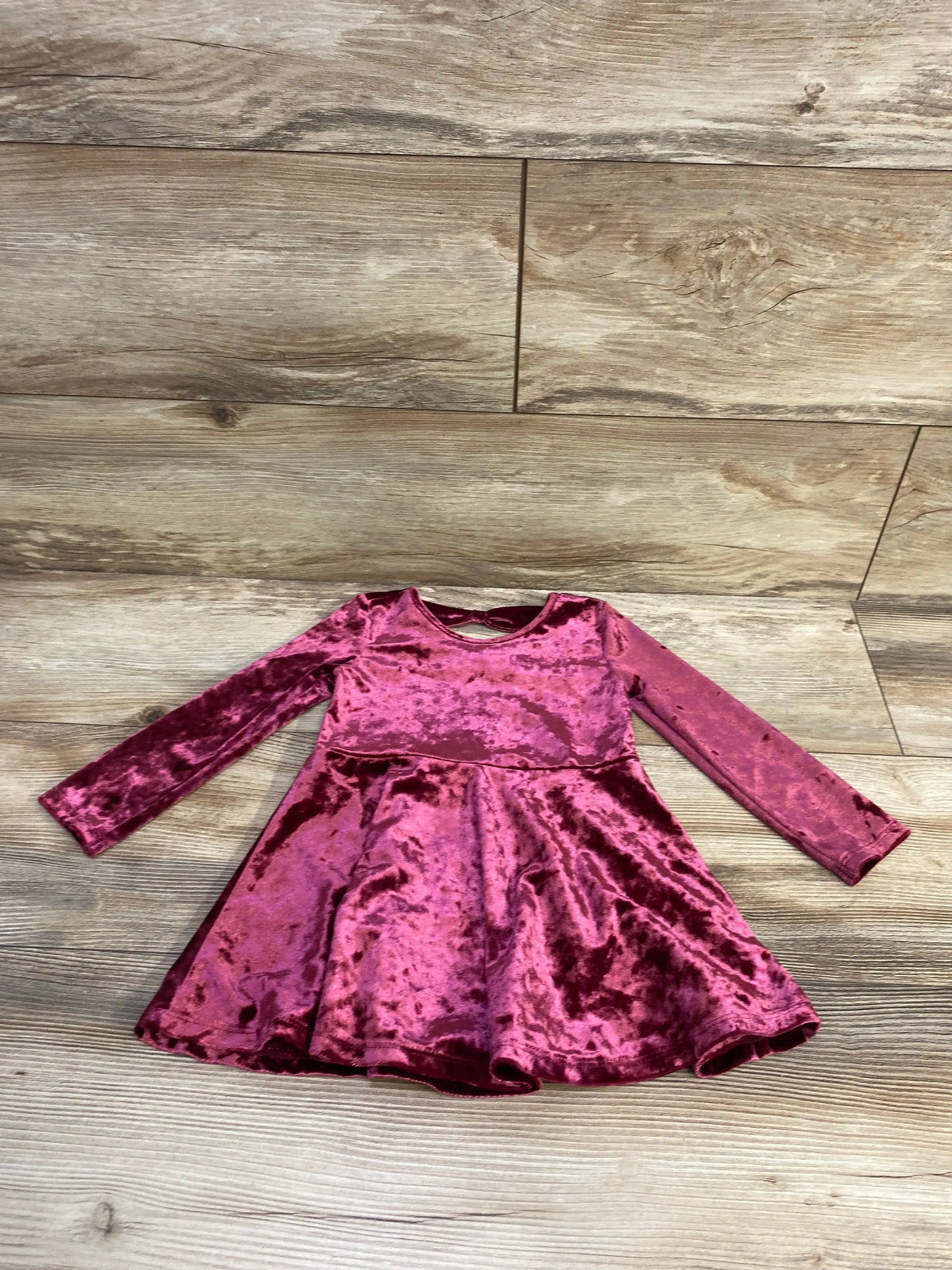 Front view of Children’s Place burgundy crushed velvet dress with long sleeves, round neckline, and flared skirt on a wood floor