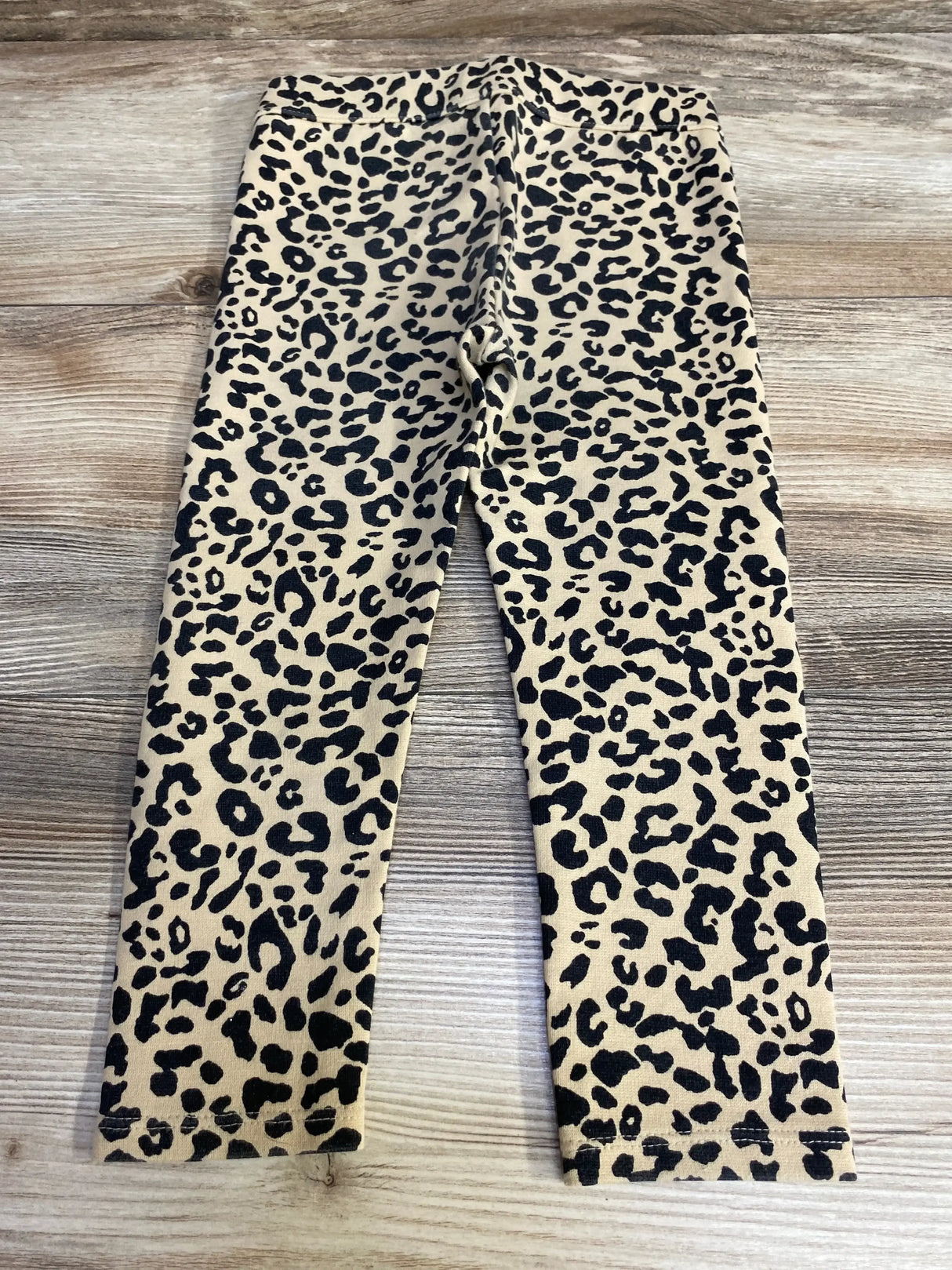 Front flat-lay of Janie and Jack toddler leopard-print leggings size 2T showing beige fabric with black spots on wood background