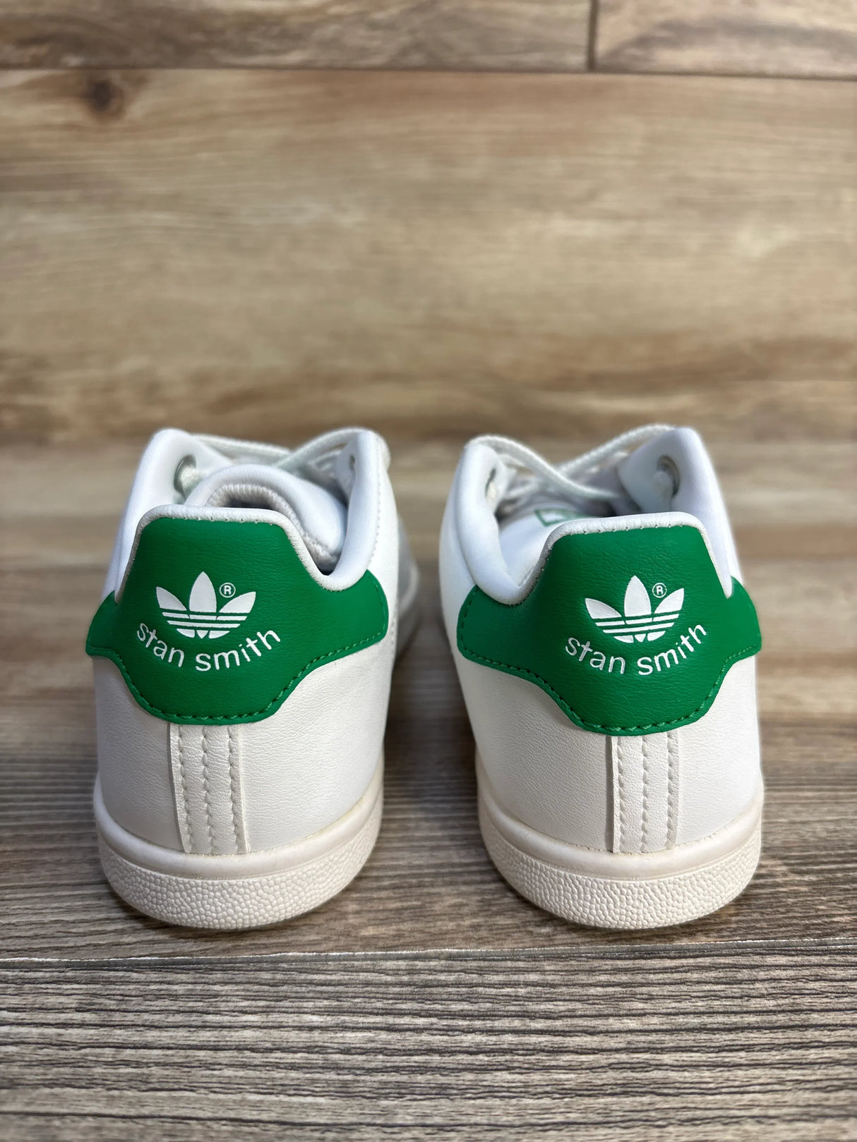 White and green Adidas Stan Smith kids sneakers on wood floor, back view