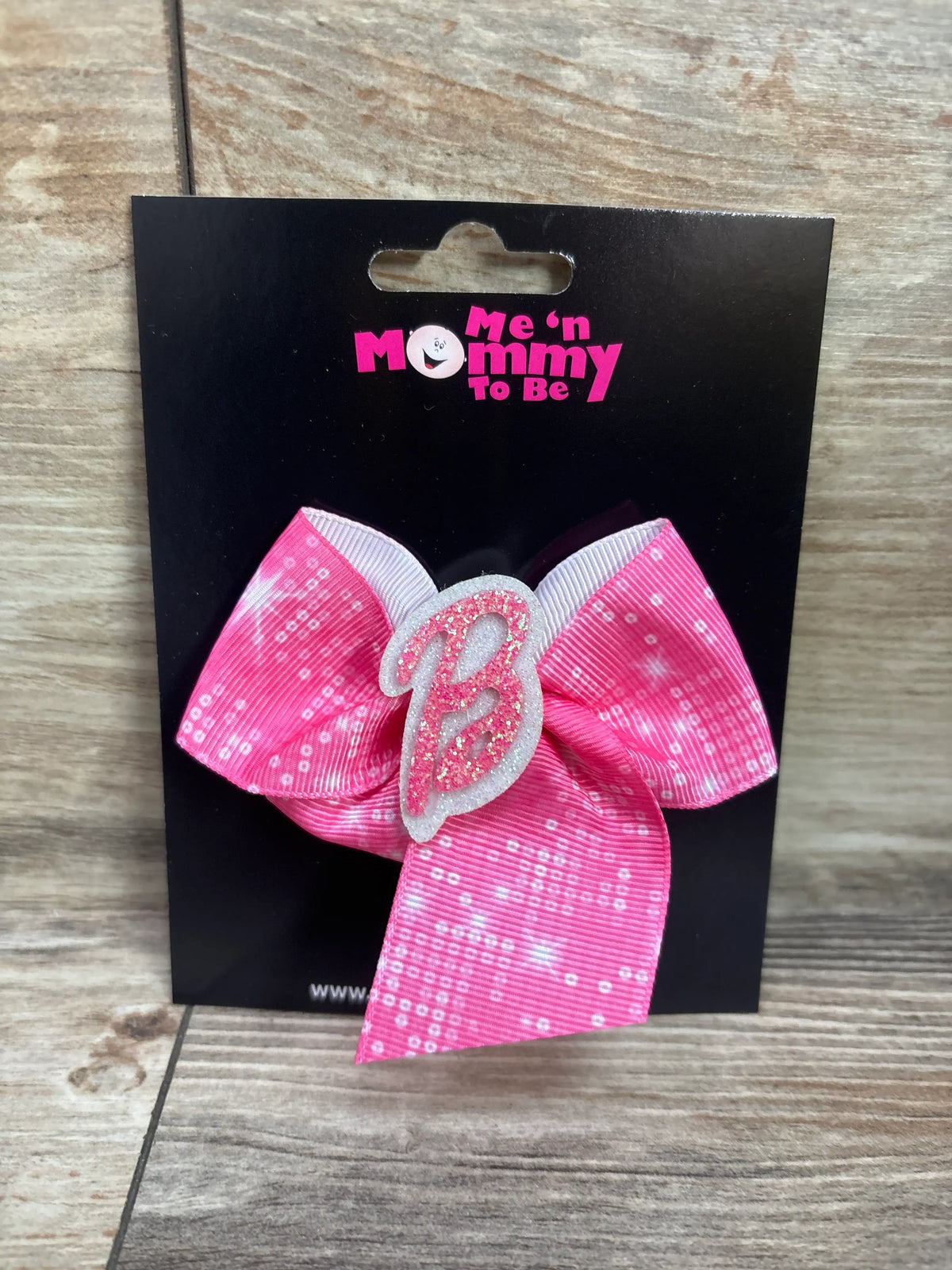 Front view of a Barbie hair bow showcasing a glittery pink B and dotted ribbon with a black display card