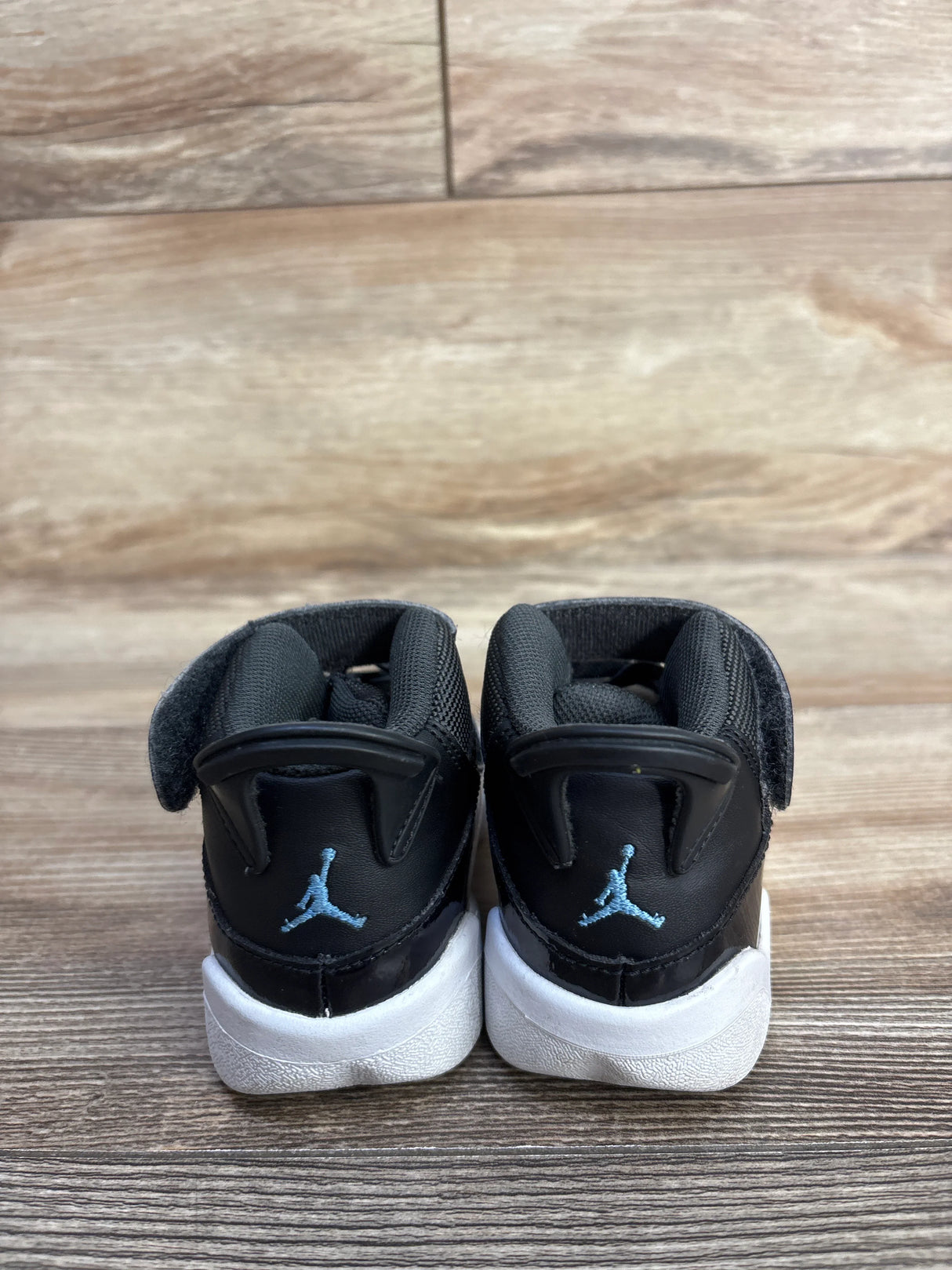 Black toddler Air Jordan sneakers with blue Jumpman logo on wooden floor