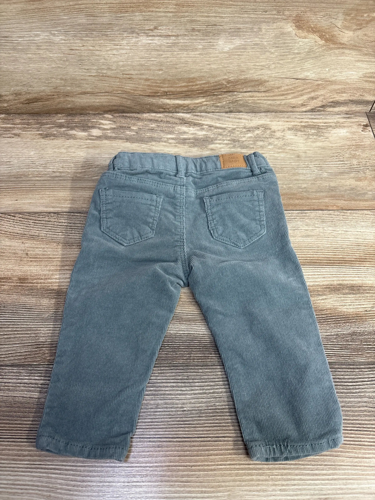Gray corduroy baby pants with back pockets, laid flat on wood surface