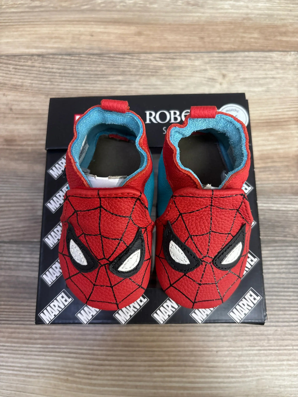 Red and blue Spider-Man themed baby shoes on Marvel-branded box on wooden surface