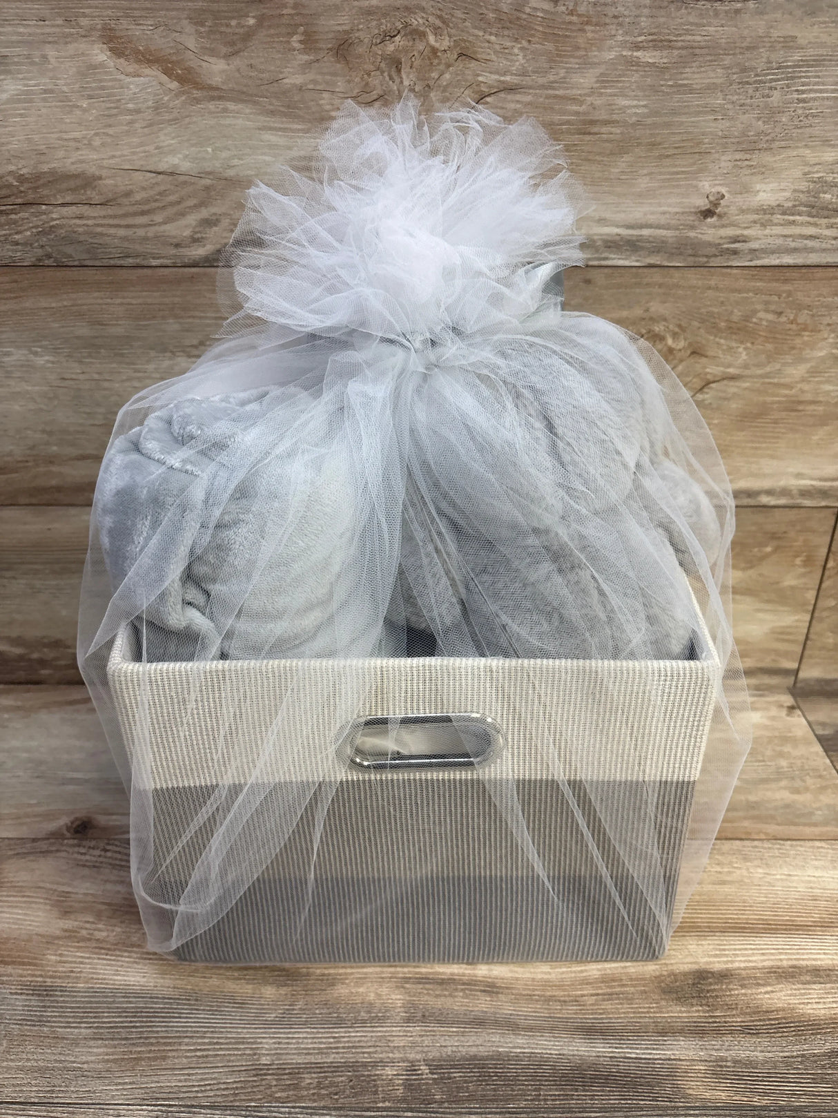 Front view of Lambs & Ivy gray baby gift basket with fabric storage bin, gray plush blanket and tulle bow on wood backdrop
