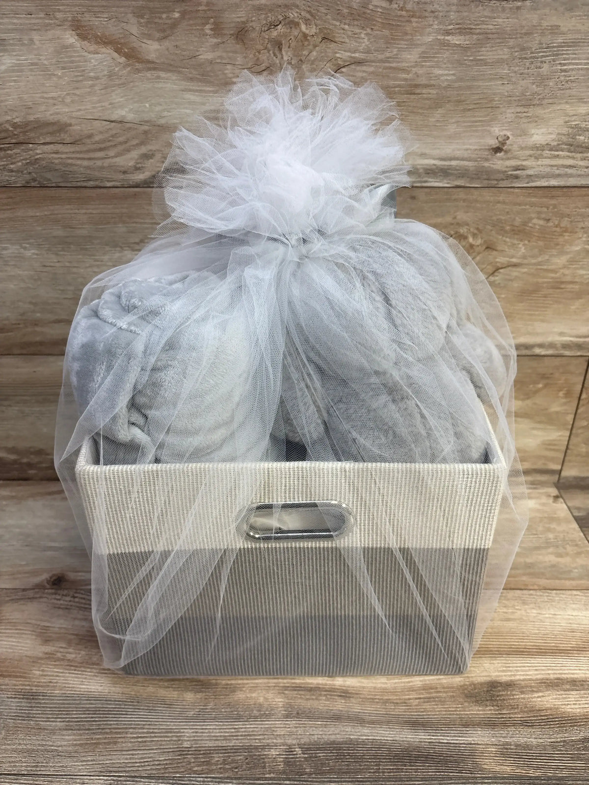 Front view of Lambs & Ivy gray baby gift basket with fabric storage bin, gray plush blanket and tulle bow on wood backdrop