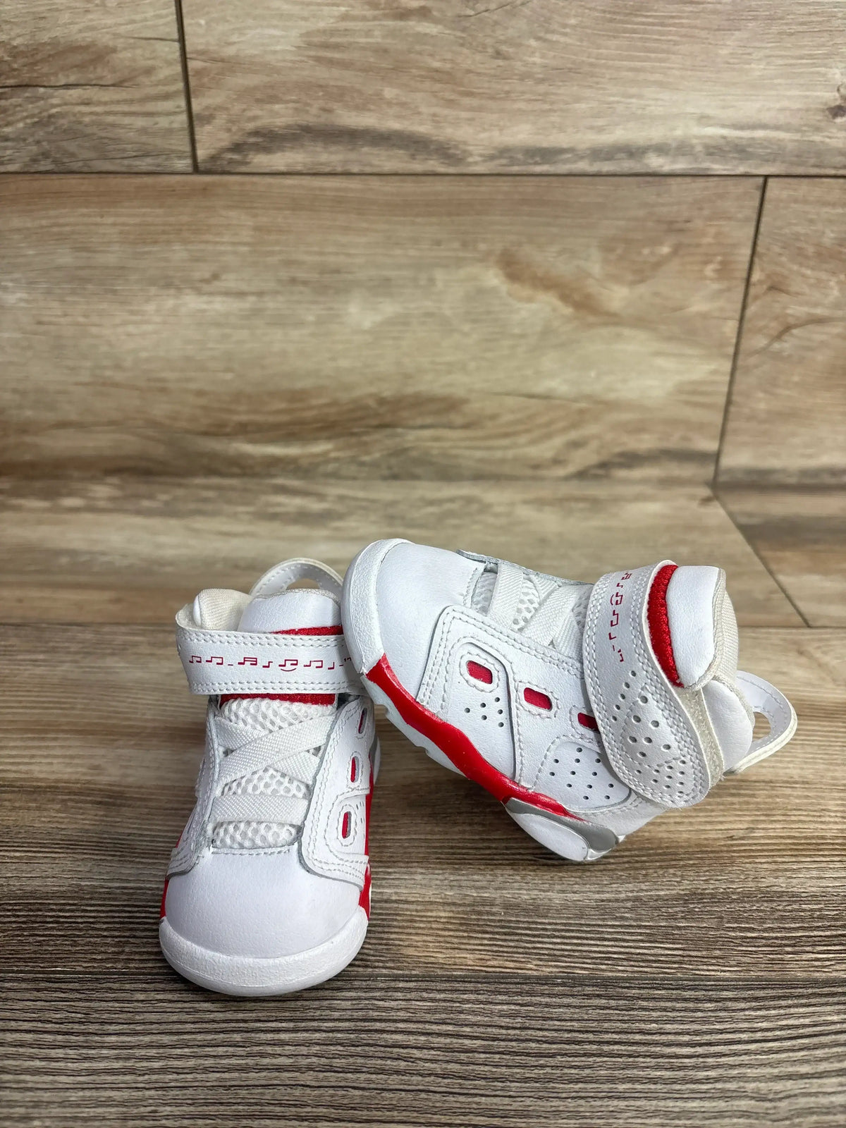 Angled front view of Air Jordan 6-17-23 (TD) toddler sneakers, white with University Red accents and Velcro strap closure on a wooden floor