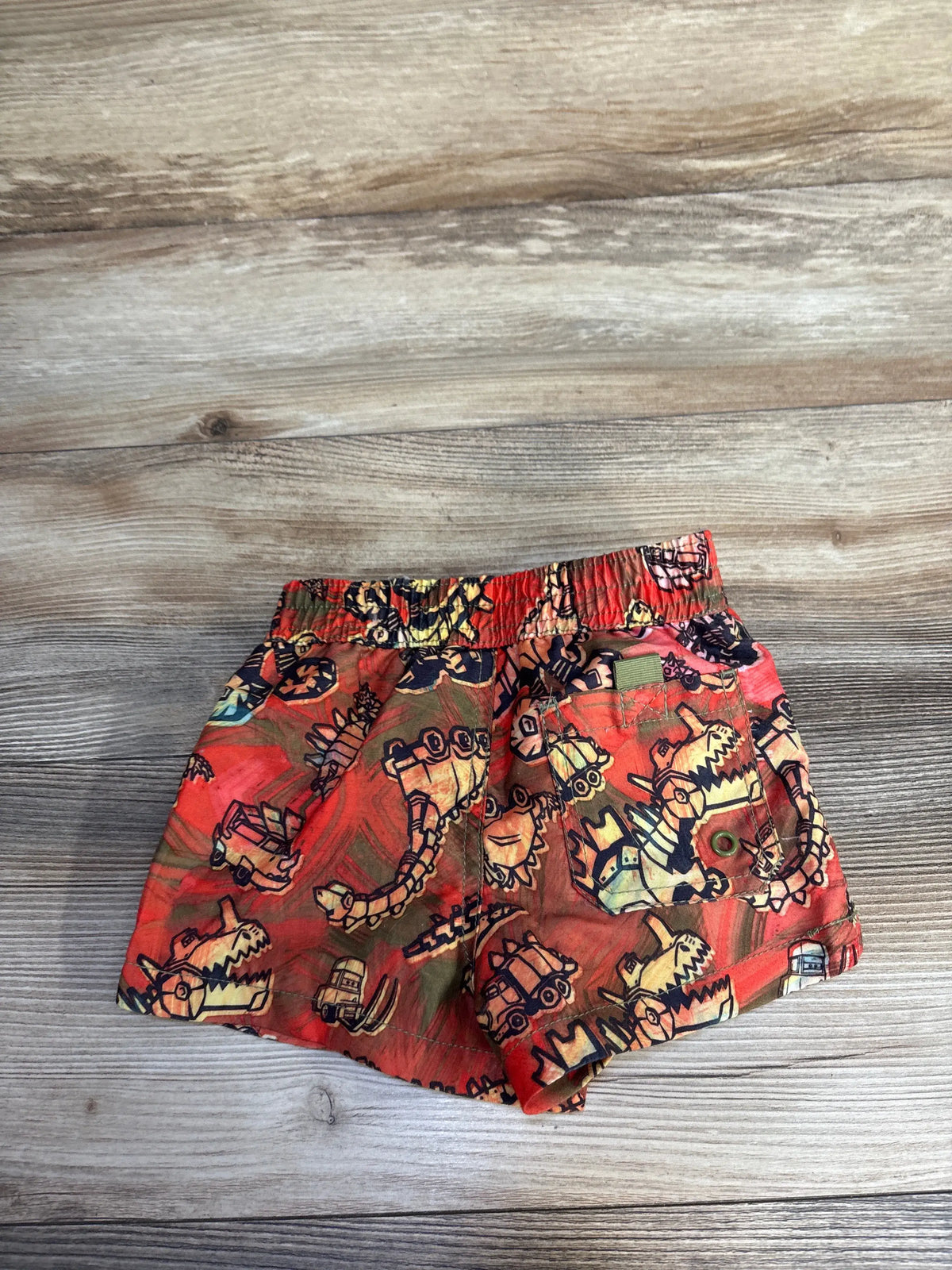 Front view of red Disney Pixar Cars swim trunks in size 2T, showcasing character graphics and elastic waistband on wood grain