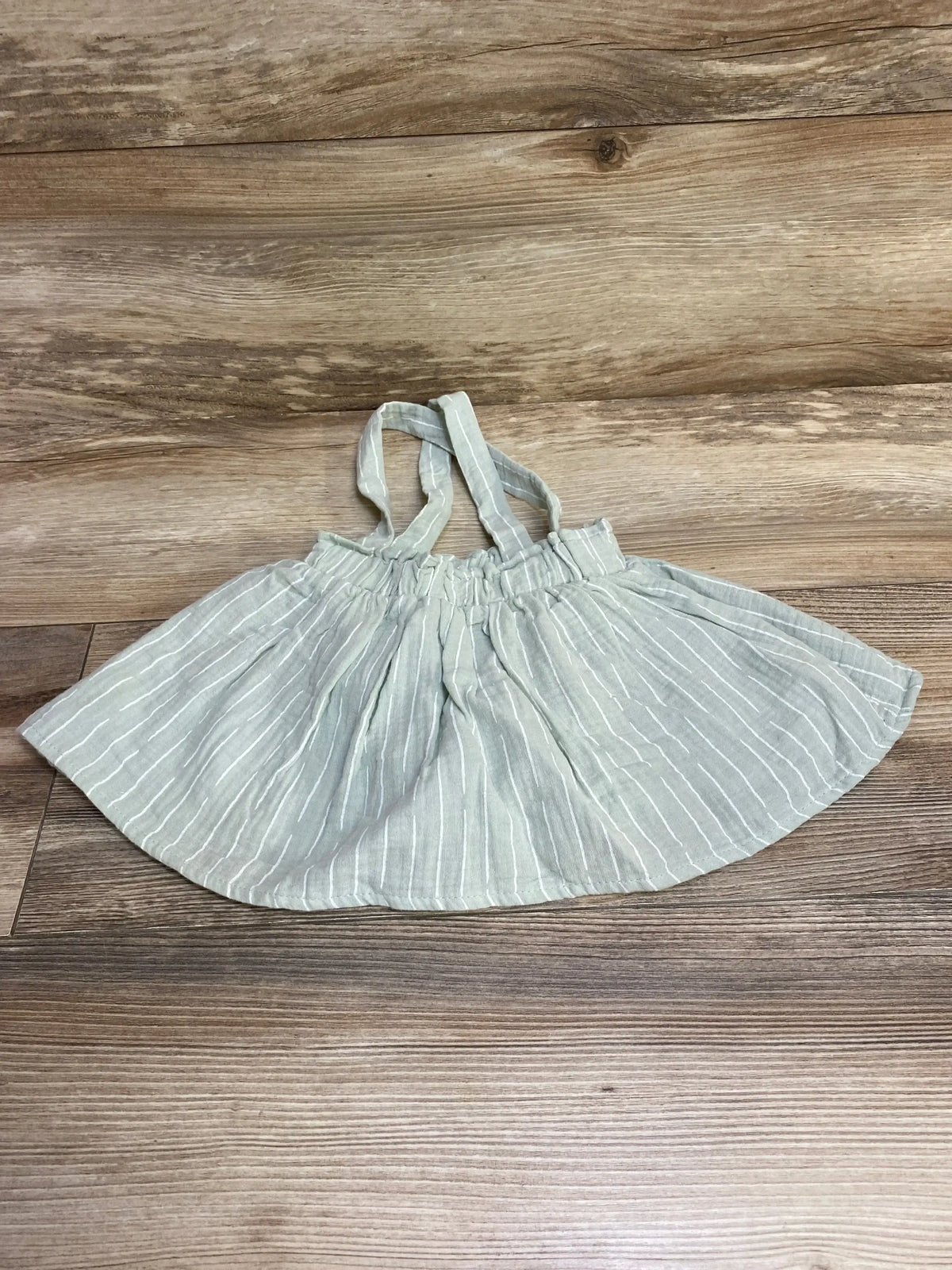 Flat lay of green striped baby skirt with attached straps and elastic waistband on wood floor