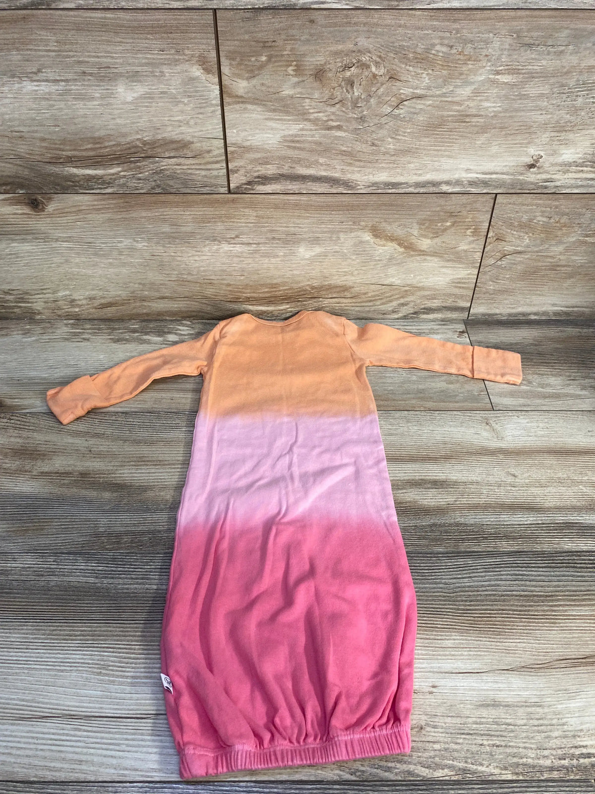 Overhead view of Honest Baby organic sleep gown showcasing orange-to-pink ombre, long sleeves and elastic hem on wood flooring