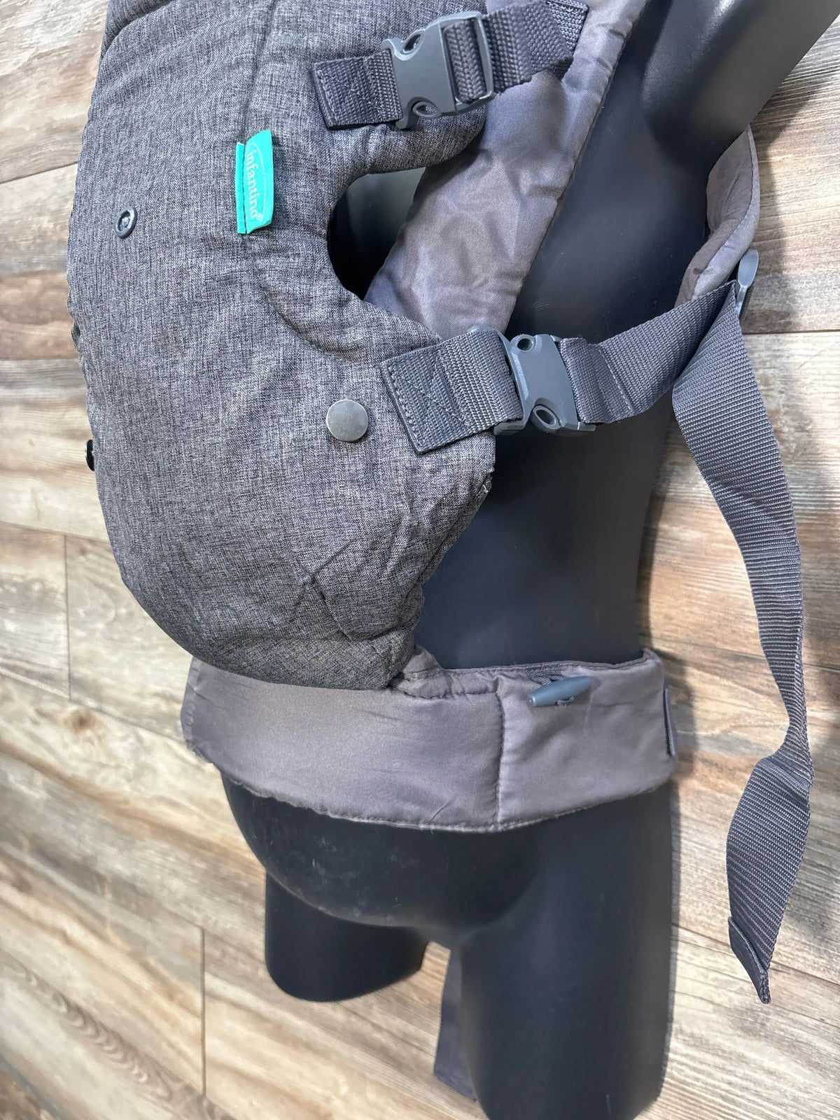 Top view of Infantino Flip 4-in-1 baby carrier showcasing grey fabric, padded waist belt, and buckled straps on wood floor