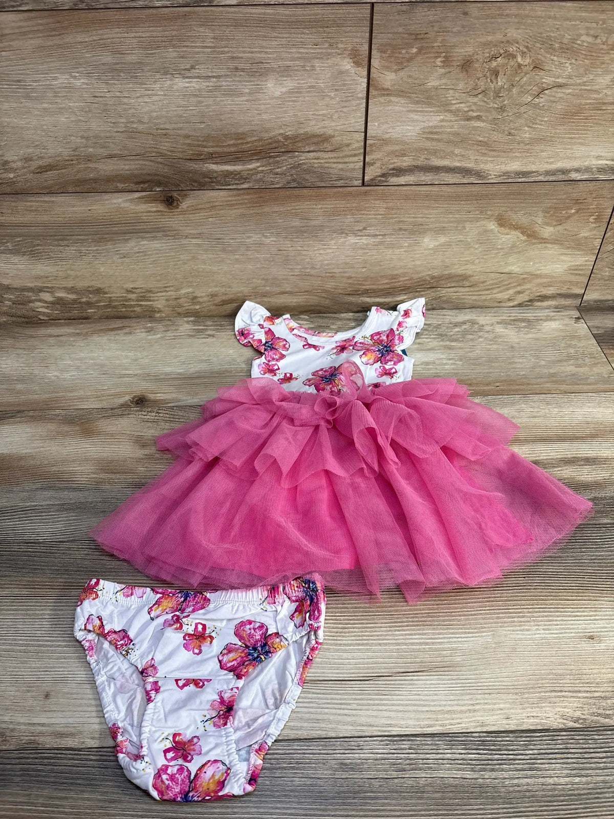 Flat lay of white toddler tutu dress with pink layered tulle skirt and matching floral bloomers, 18-24 months, on light wood background