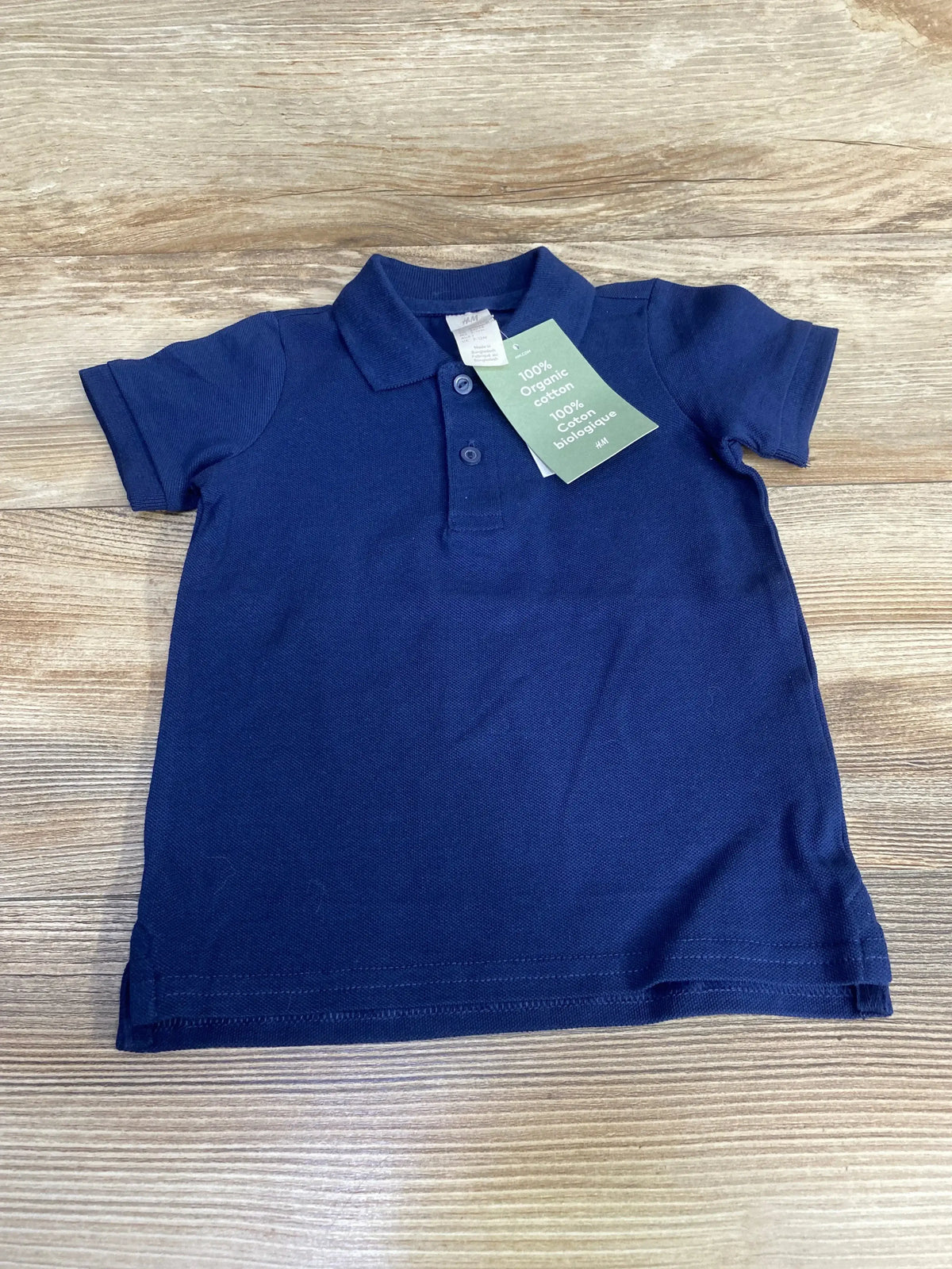 Flat lay of H and M navy polo shirt size 12 months showcasing two-button placket and short sleeves with light wood background