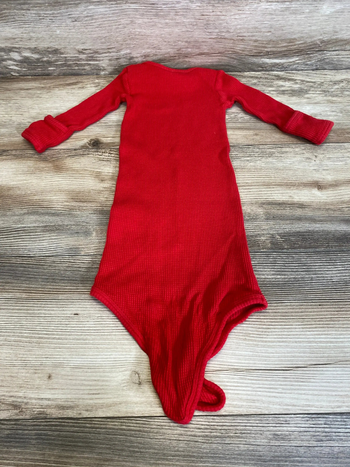 Flat lay of red waffle-knit knotted baby gown showcasing long sleeves and knotted hem on light wood background