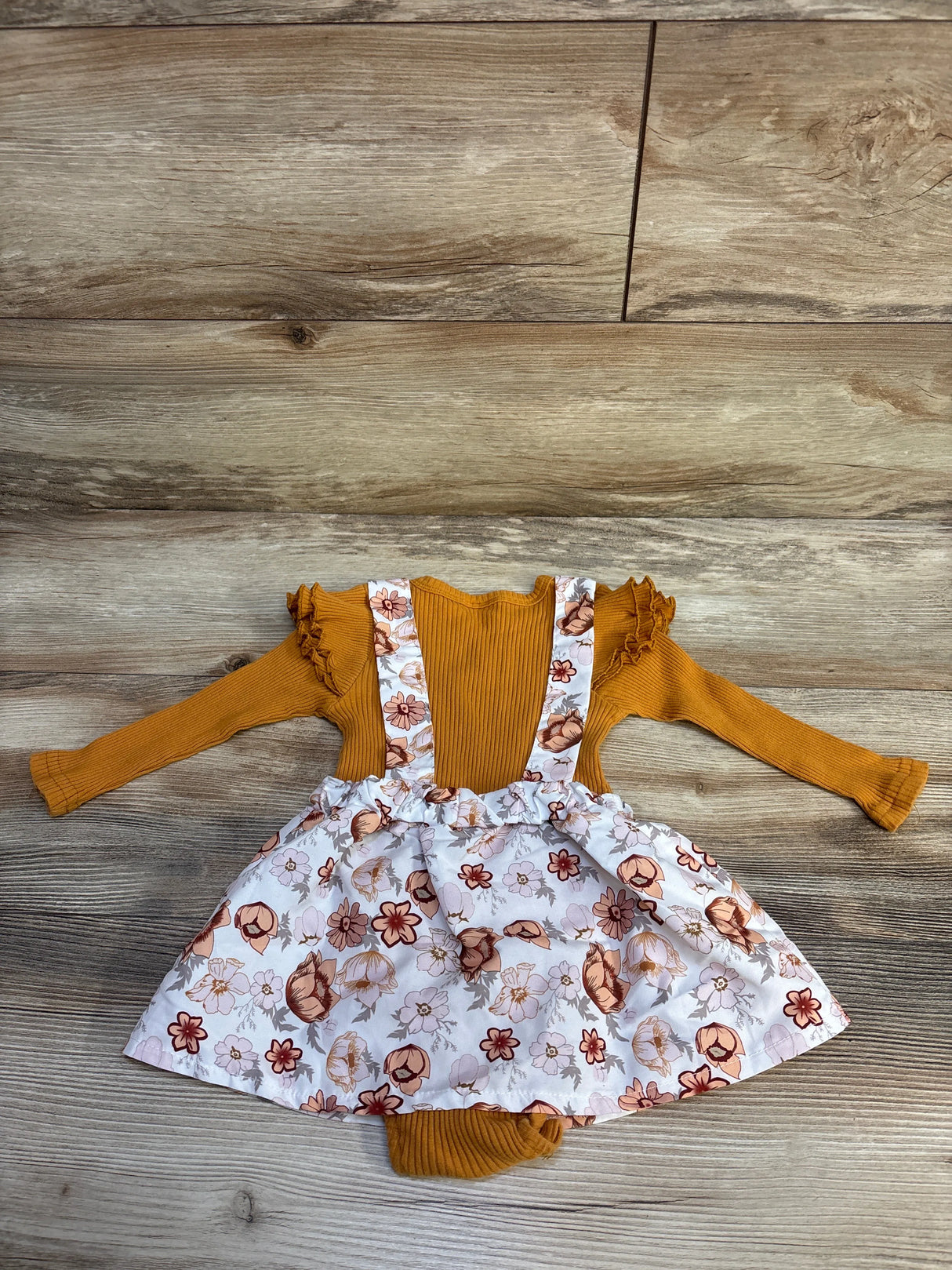 Mustard yellow long-sleeve baby romper with floral print suspender skirt on wooden floor