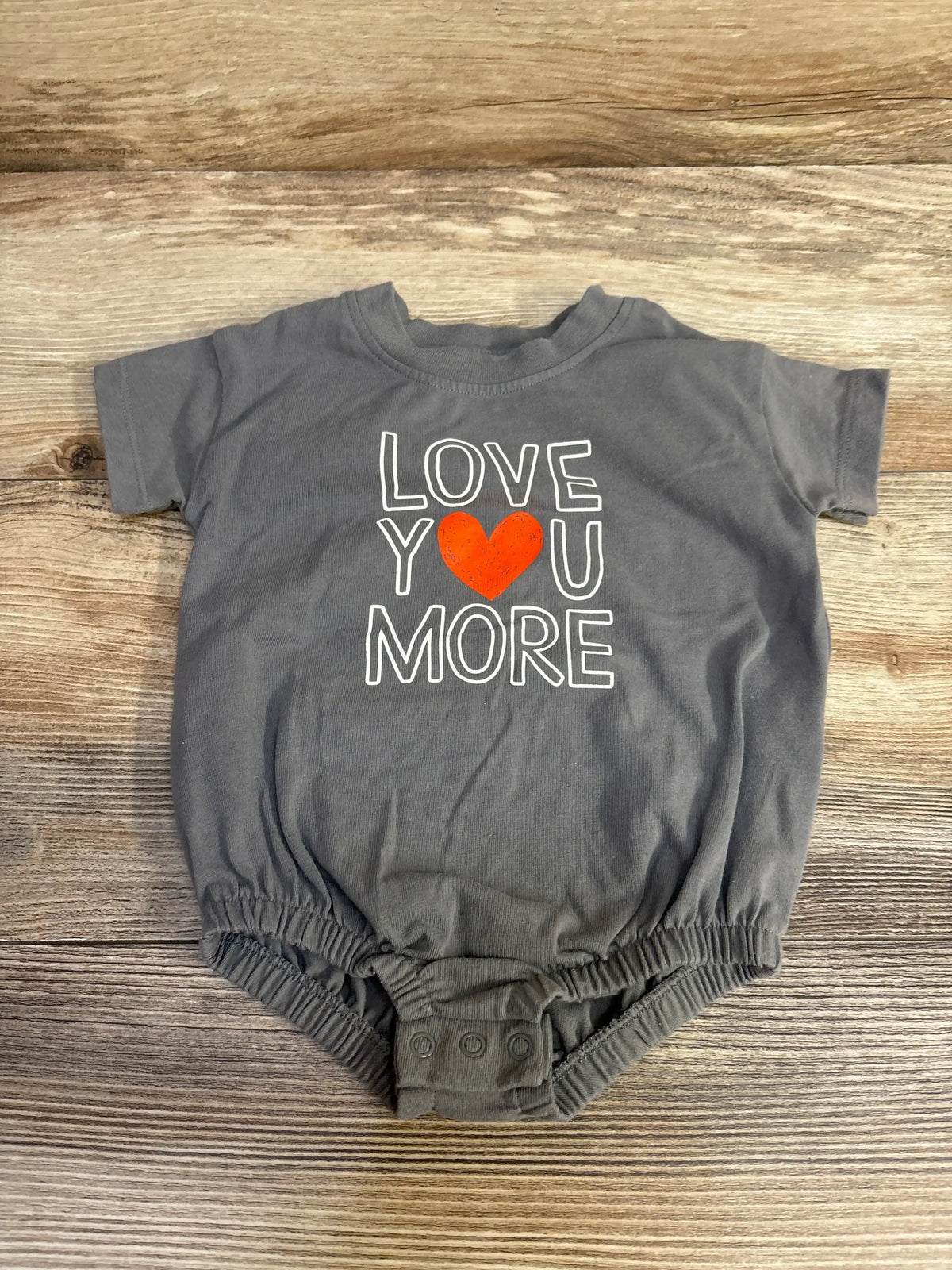 Flat lay of grey newborn romper (0-3M) with LOVE YOU MORE print and orange heart, snaps at crotch on wood background