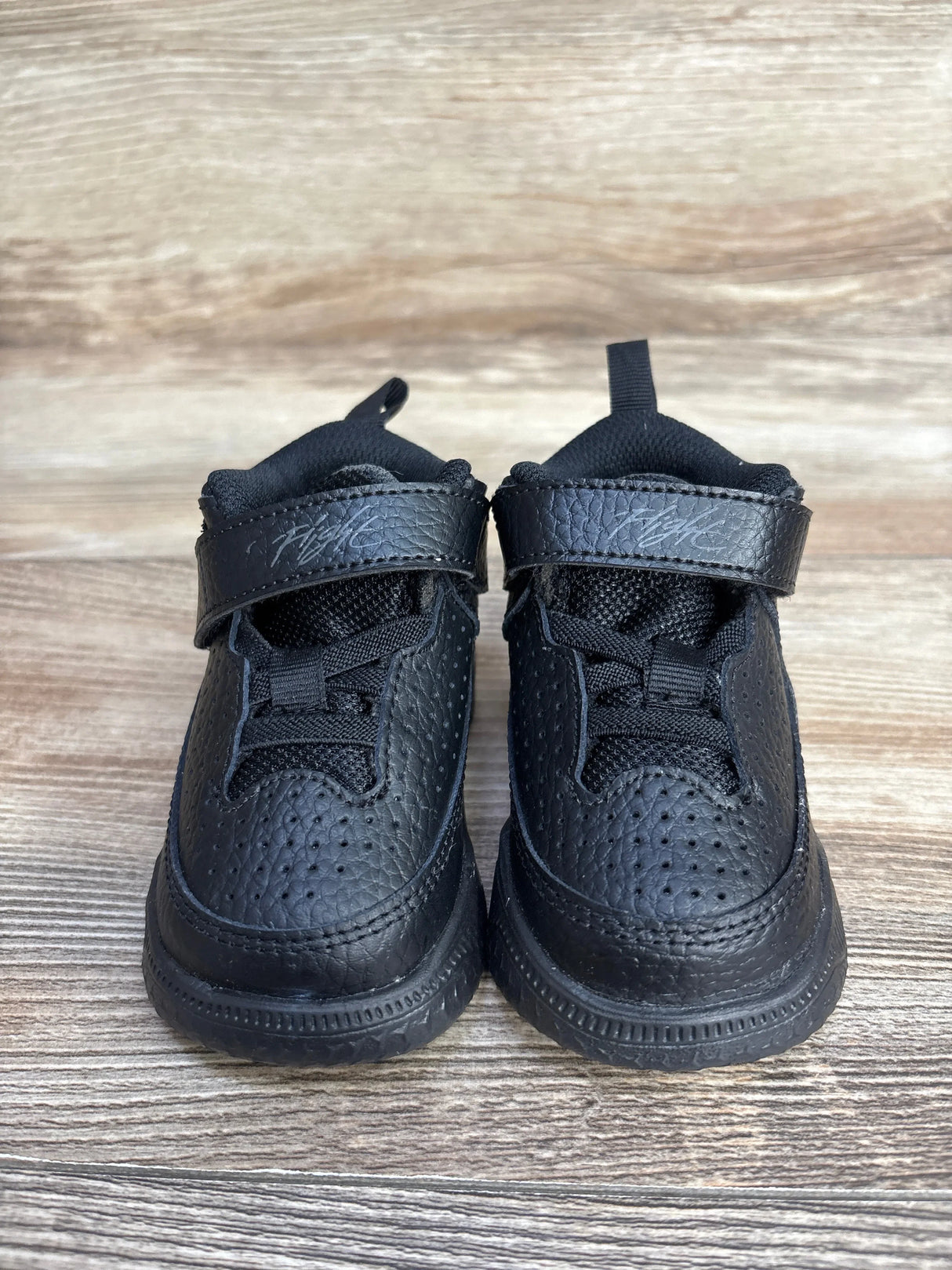 Pair of black toddler sneakers with Velcro straps labeled Flight on wooden floor