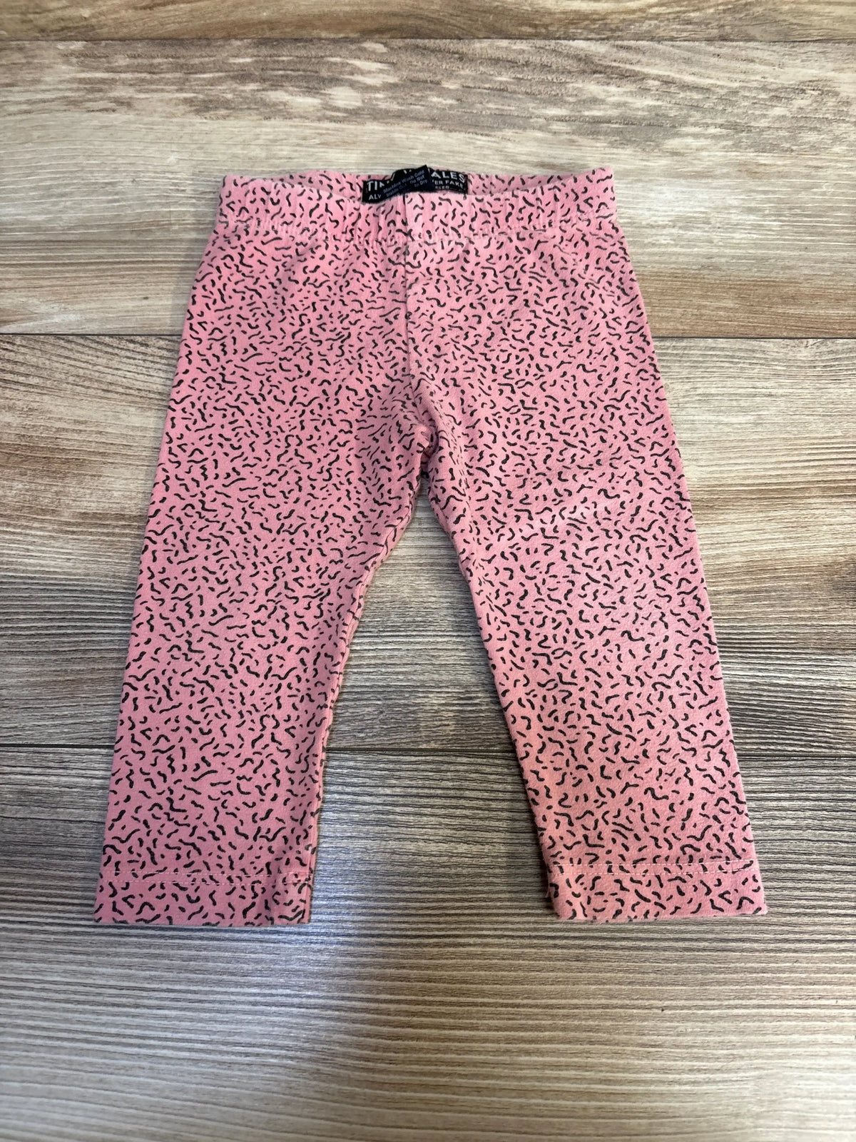 Pink toddler leggings with black squiggle pattern on wooden floor