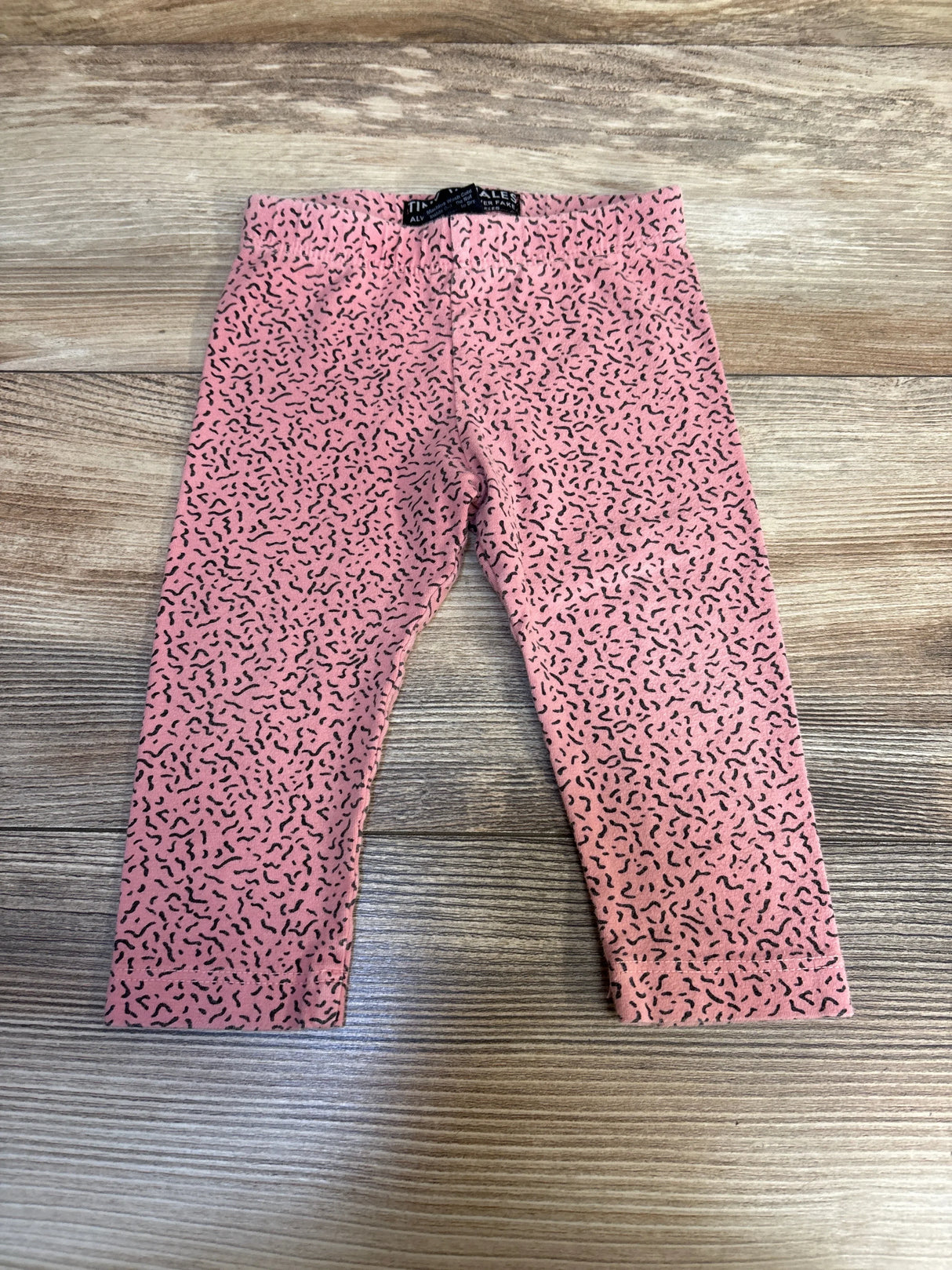 Pink toddler leggings with black squiggle pattern on wooden floor