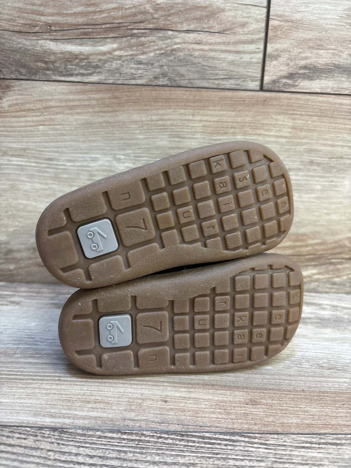 Bottom view of brown toddler shoes with textured rubber soles and size marking, on wood floor