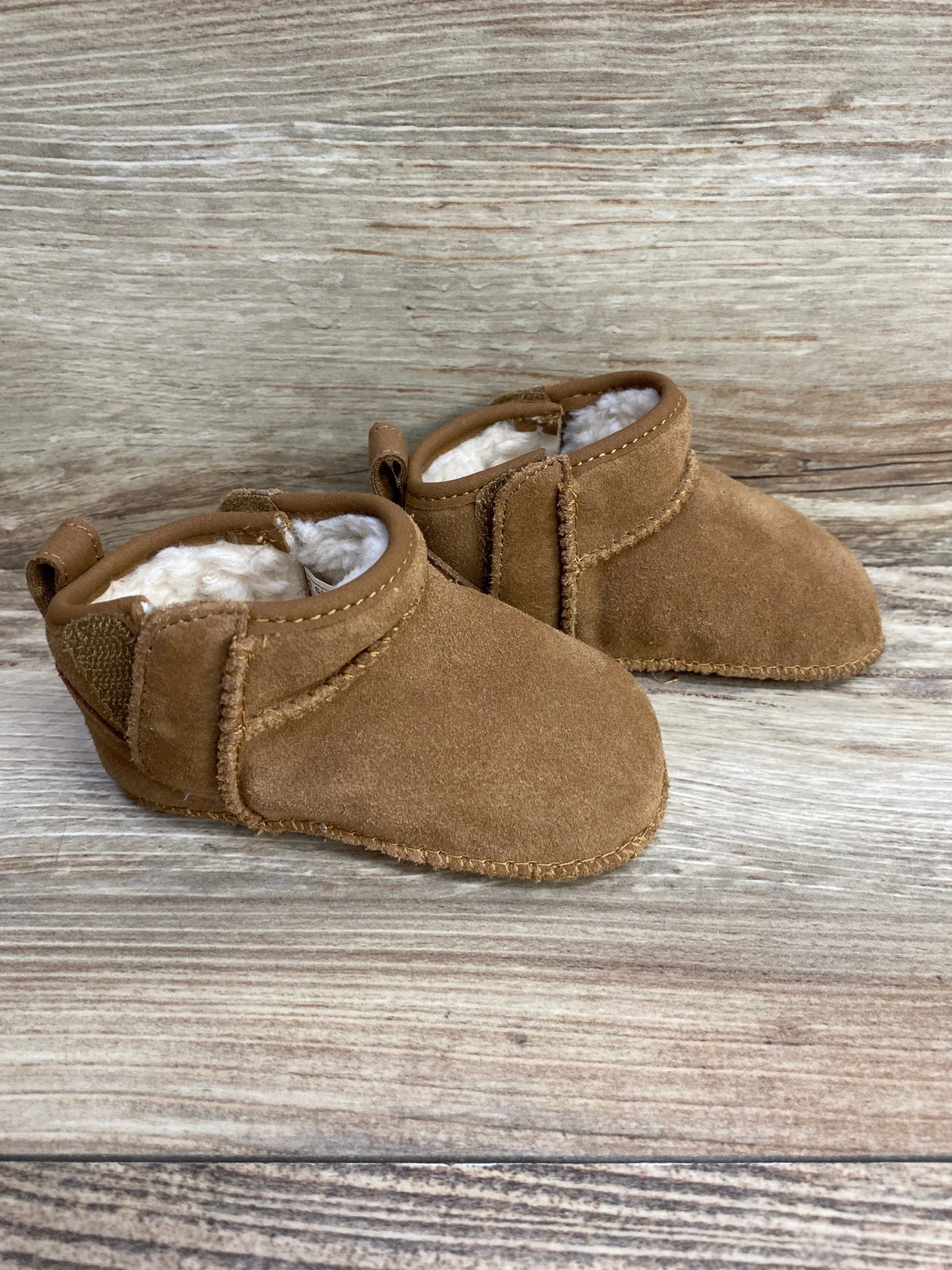 Brown suede baby booties with warm white fleece lining on wooden surface