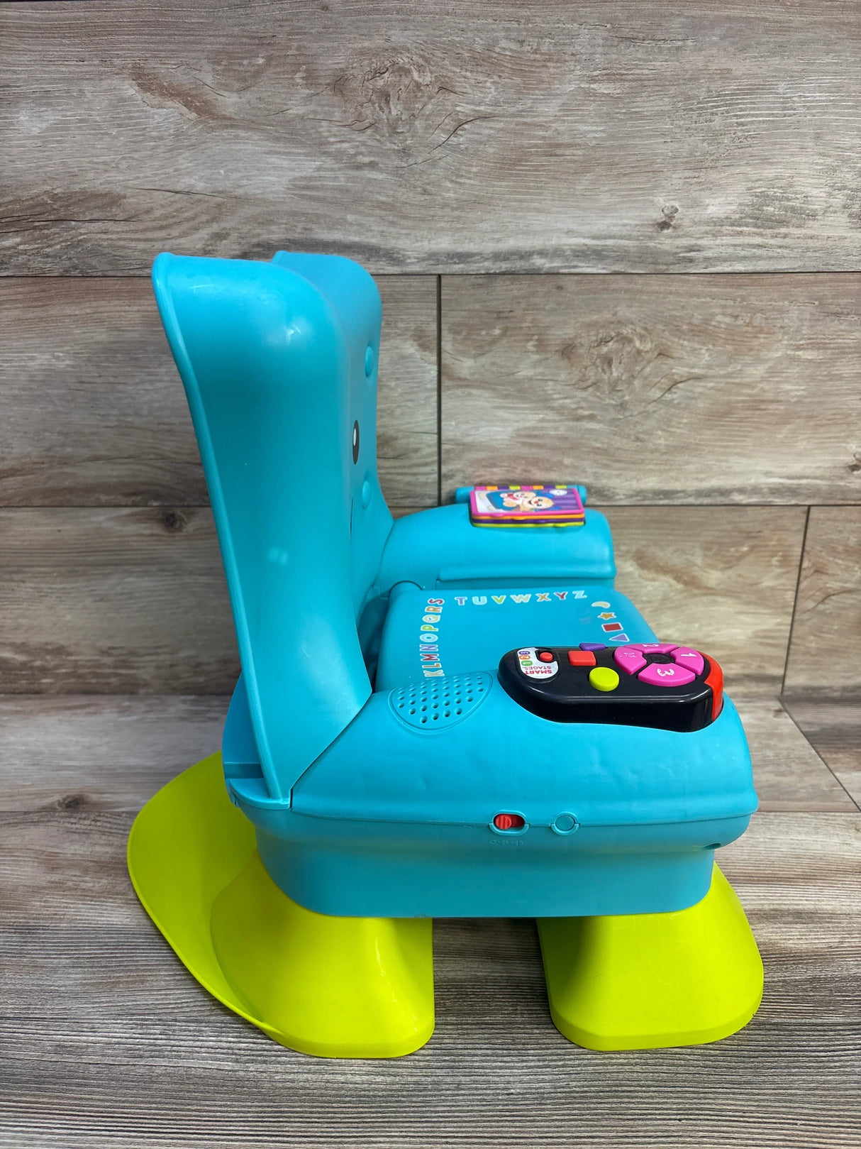 Side view of Fisher-Price Laugh and Learn teal chair with electronic buttons and flip book on yellow rocker on wood backdrop
