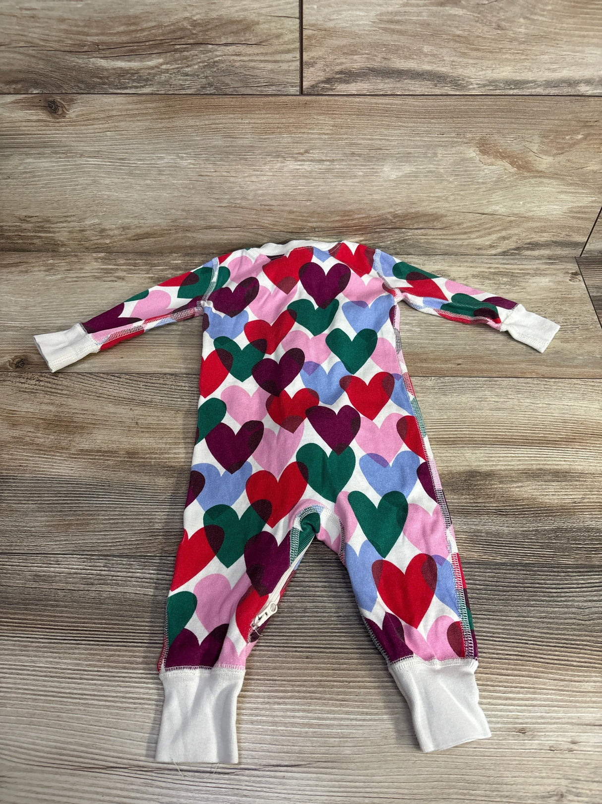 Colorful baby romper with multicolor heart pattern and white cuffs laid flat on wood floor