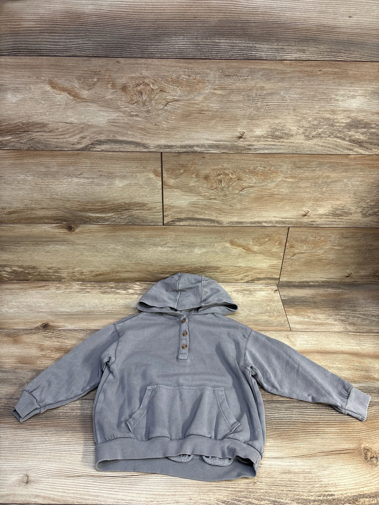 Flat-lay front of grey toddler Henley pullover hoodie showing three button placket and kangaroo pocket on wood background